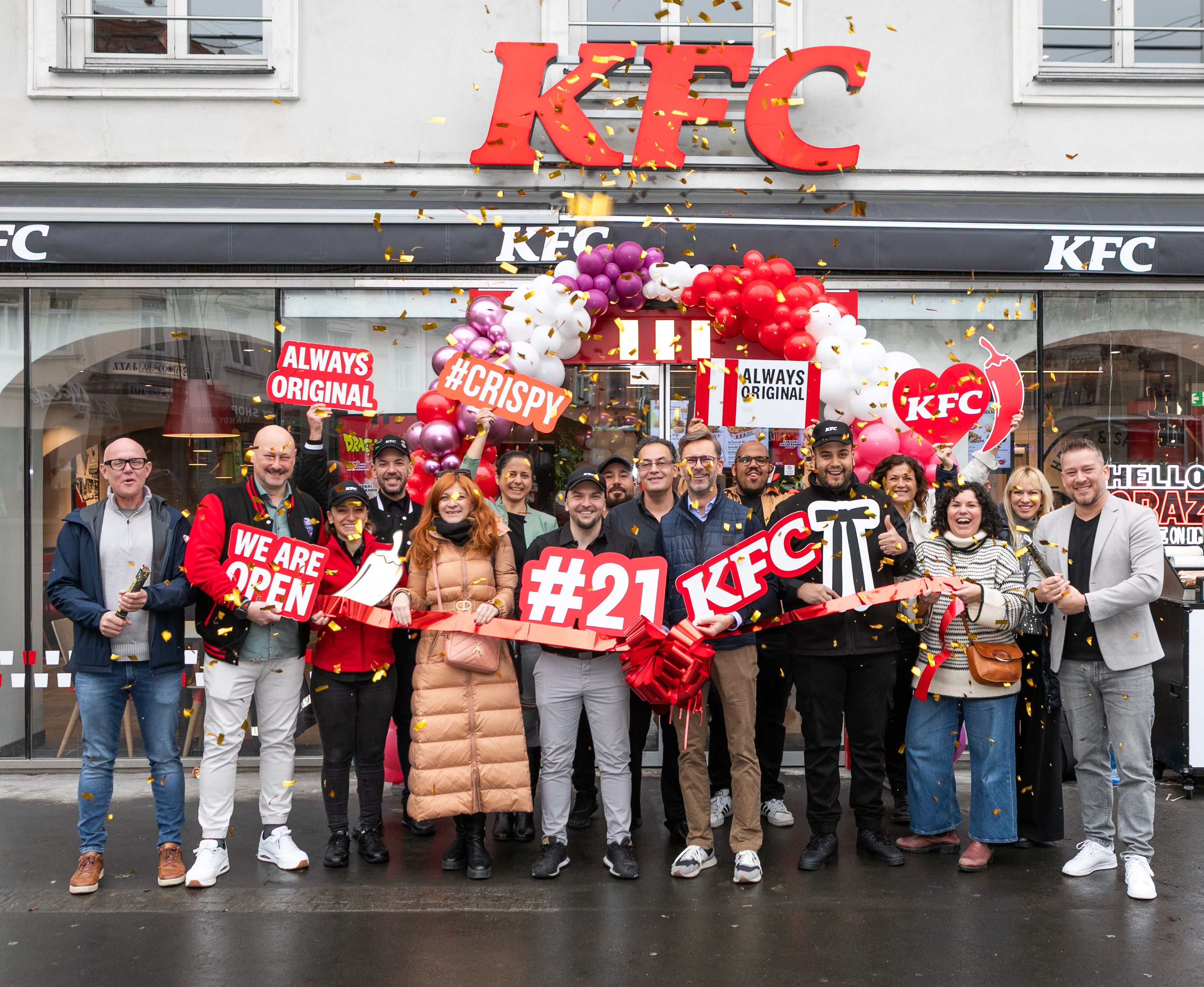 Team feiert die Neueröffnung der KFC-Filiale Graz mit Eröffnungsband und Schild 'Hello Graz'