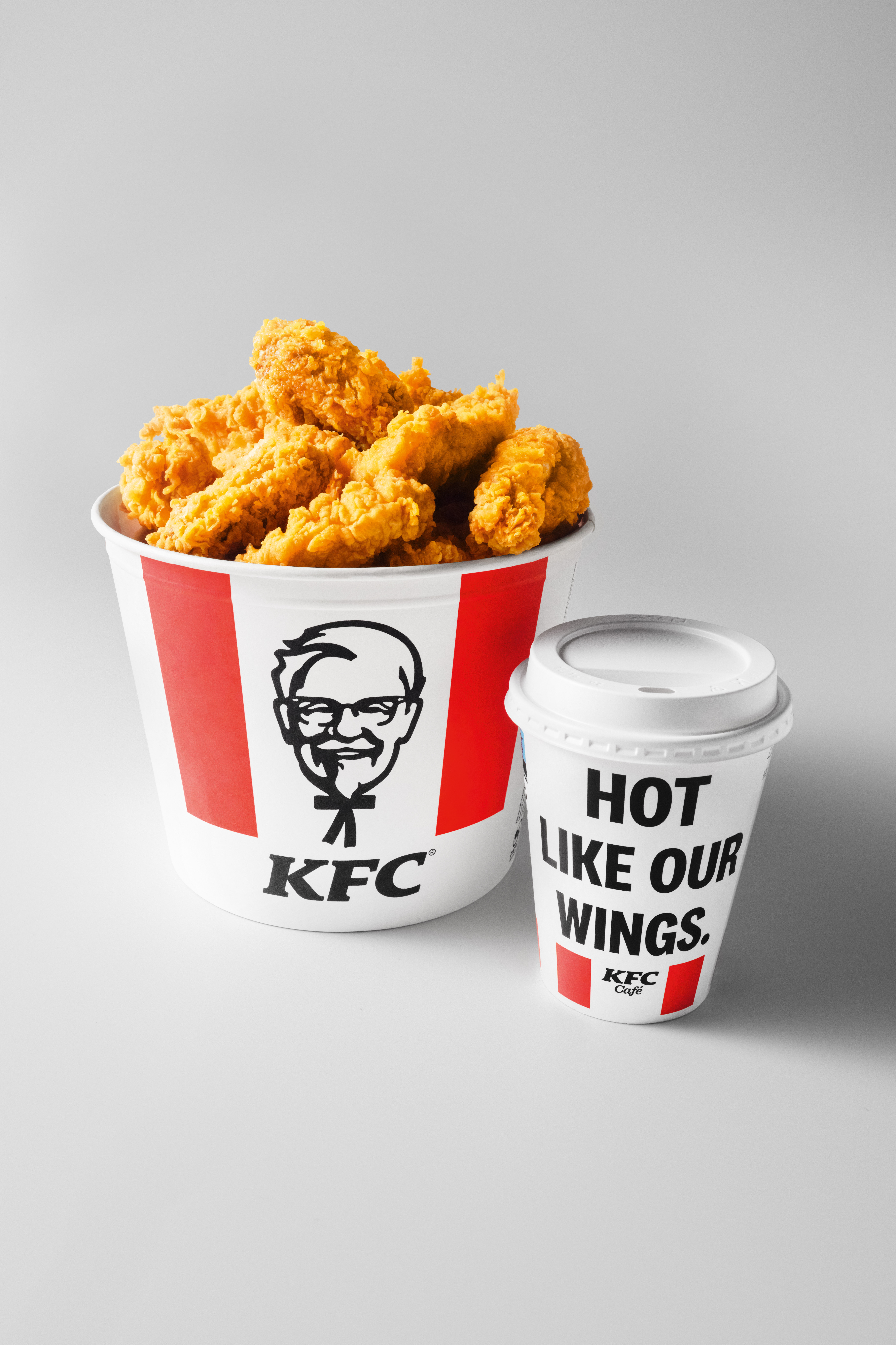 KFC-Bucket mit Chicken Strips neben einem KFC-Café-Kaffeebecher 'Hot Like Our Wings'