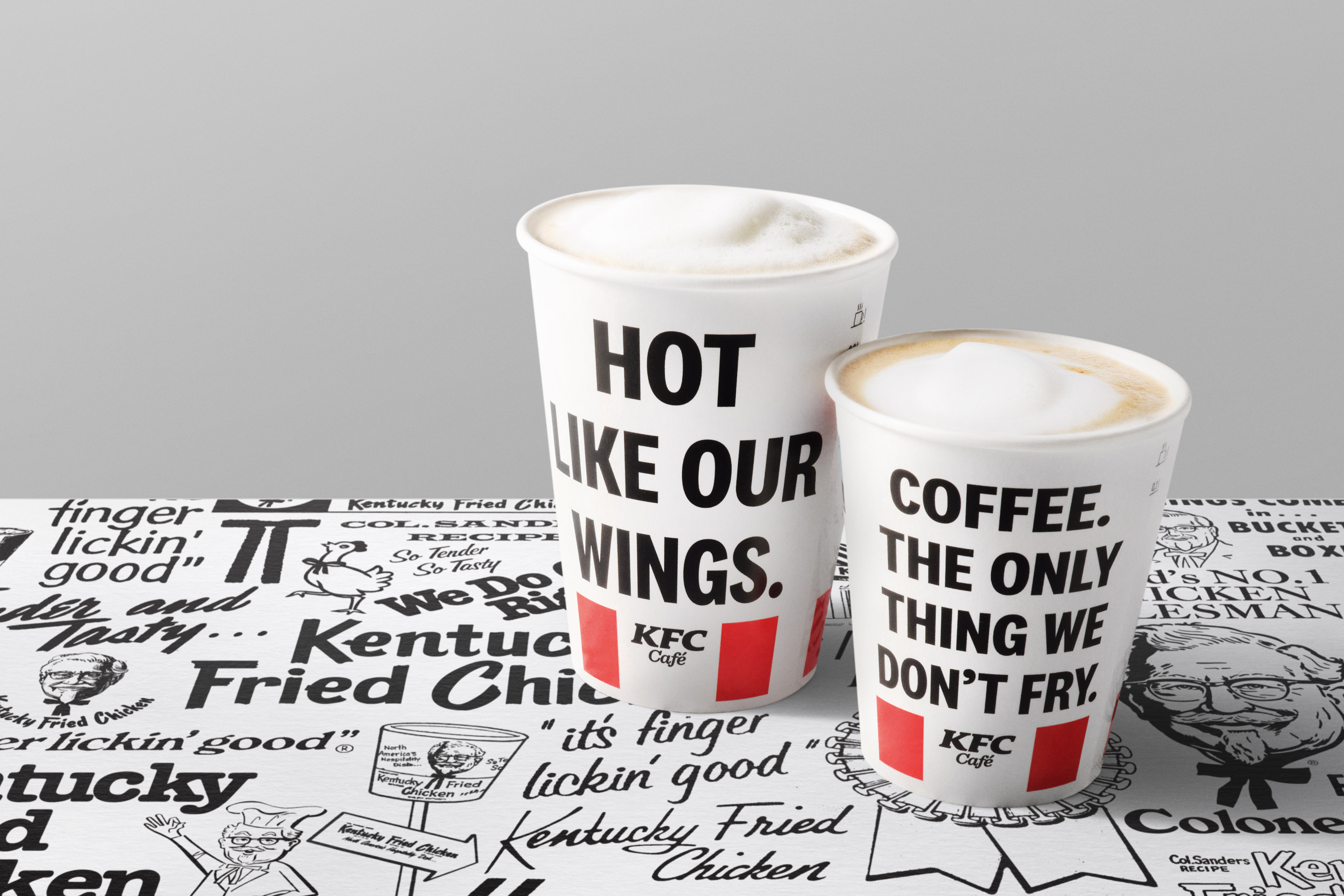 Zwei KFC-Café-Kaffeebecher auf einer mit KFC-Sprüchen bedruckten Unterlage