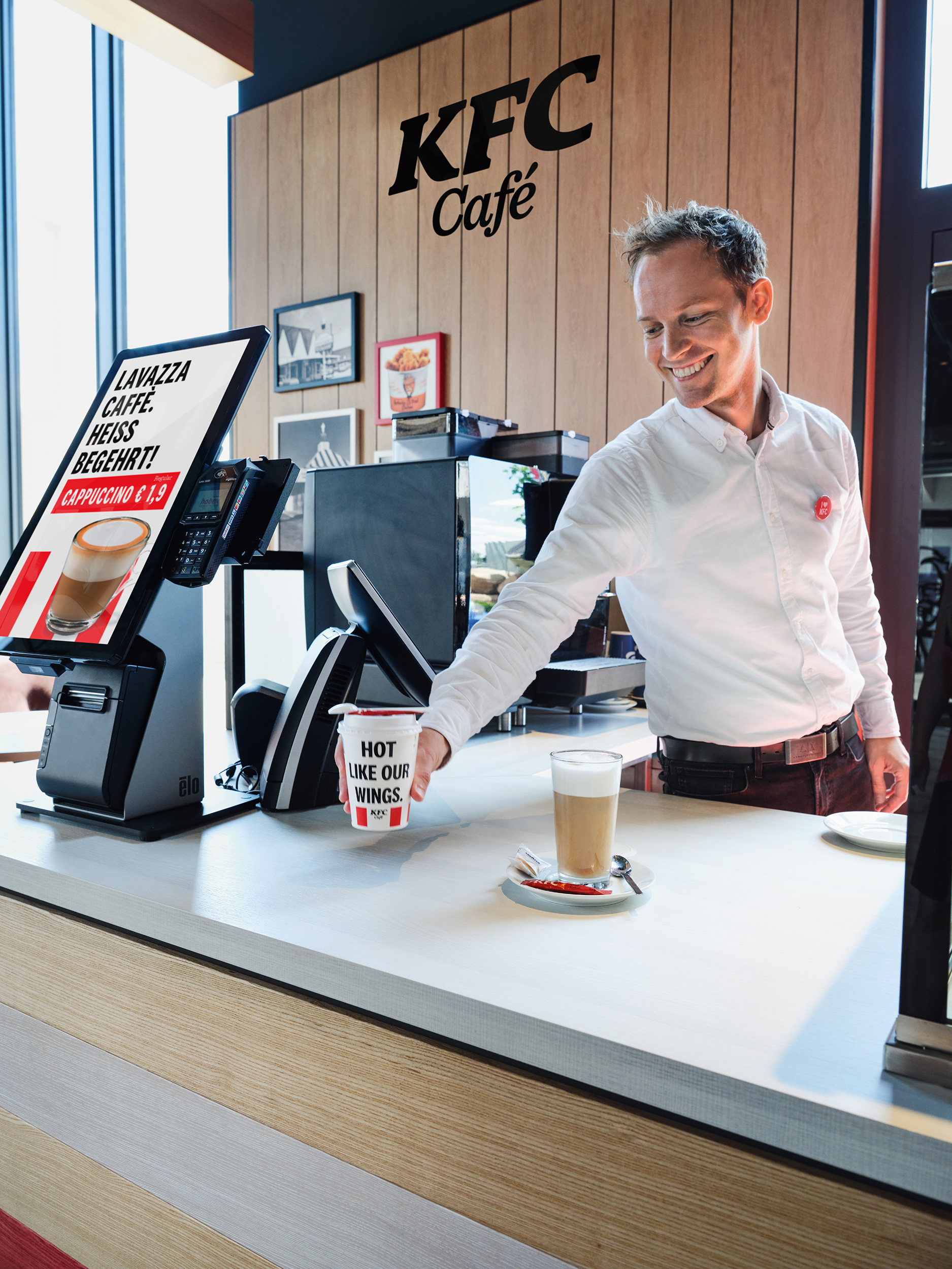 Mitarbeiter reicht am Tresen einen Kaffee im KFC Café, Milchkaffee im Vordergrund