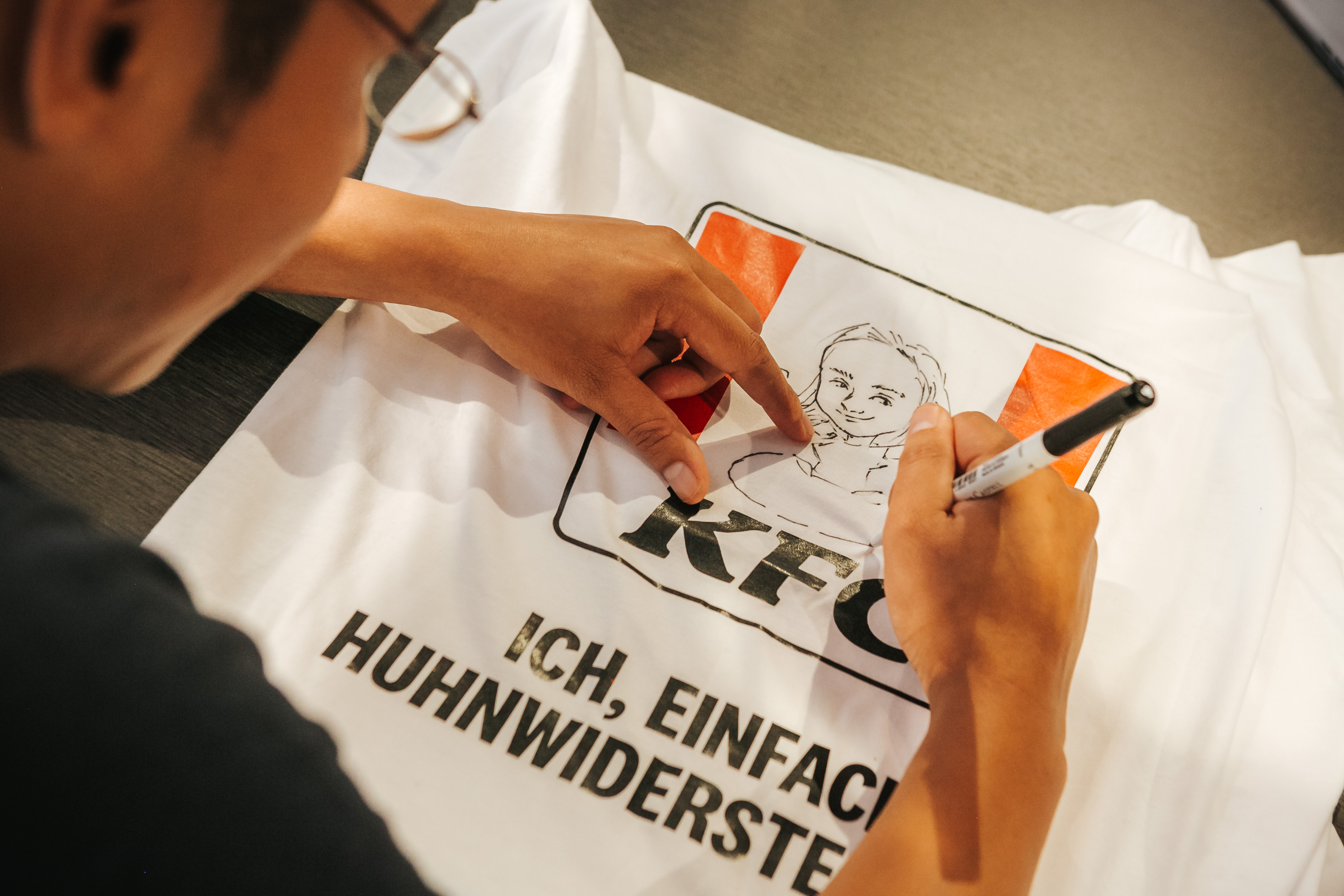 Person signiert ein KFC-T-Shirt mit gezeichnetem Colonel-Sanders-Porträt