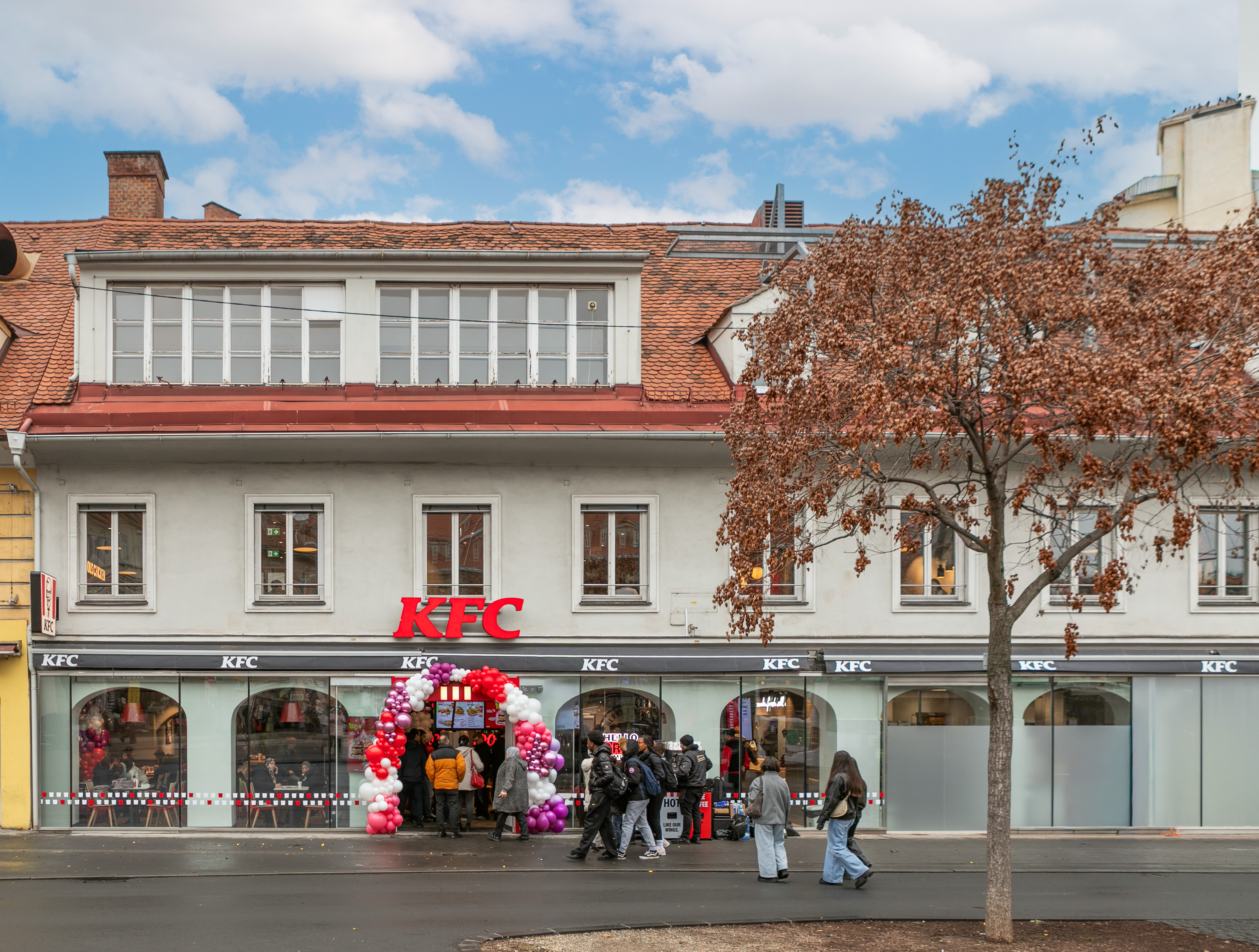 Straßenfassade der KFC-Filiale Graz mit Logo und Ballongirlande am Eingang zur Eröffnung