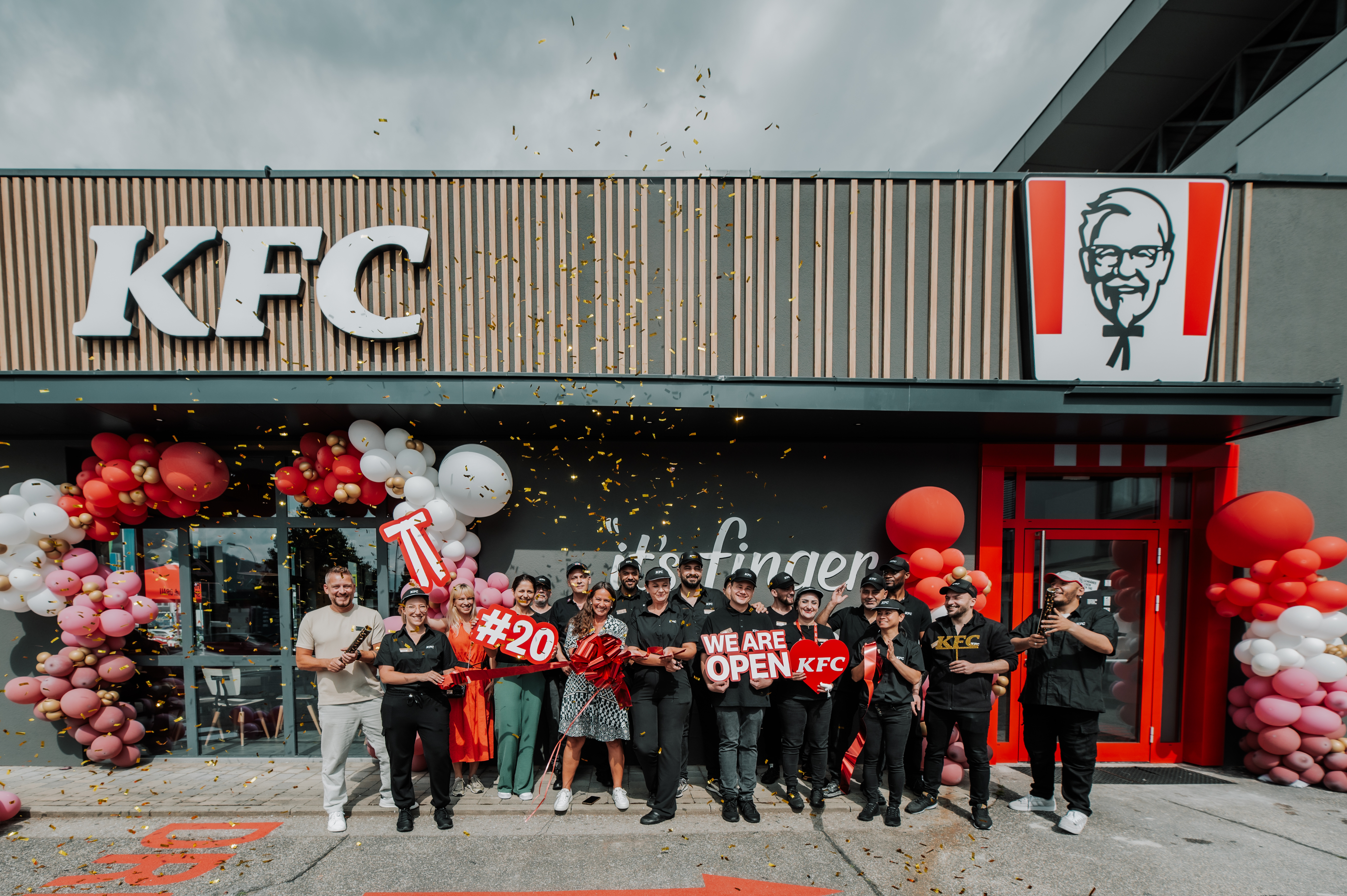 Team feiert die Neueröffnung einer KFC-Filiale mit Konfettiregen und Schild 'We Are Open'
