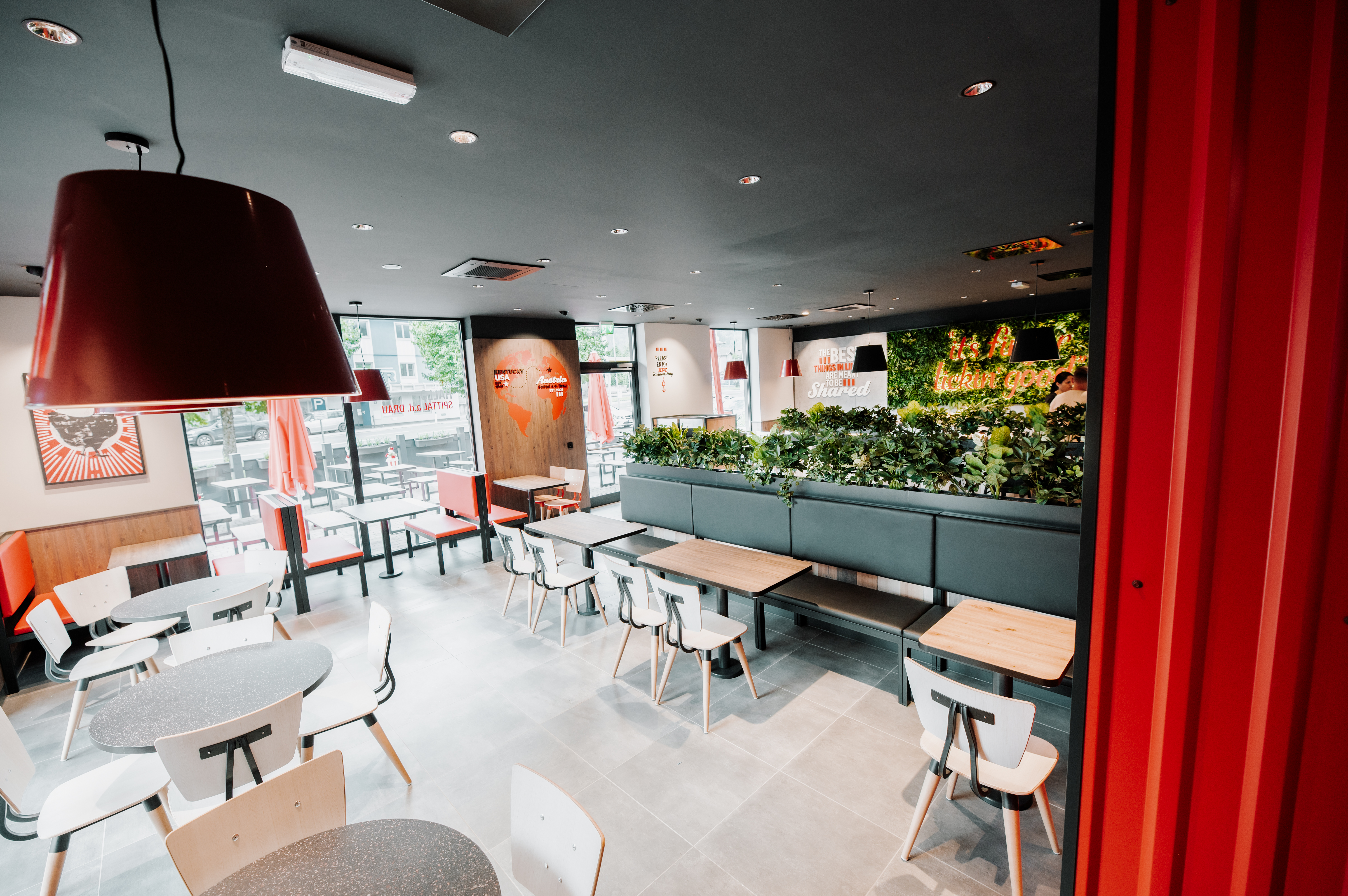 Sitzbereich einer KFC-Filiale mit weißen Stühlen, Pflanzenwand und Blick auf die Terrasse