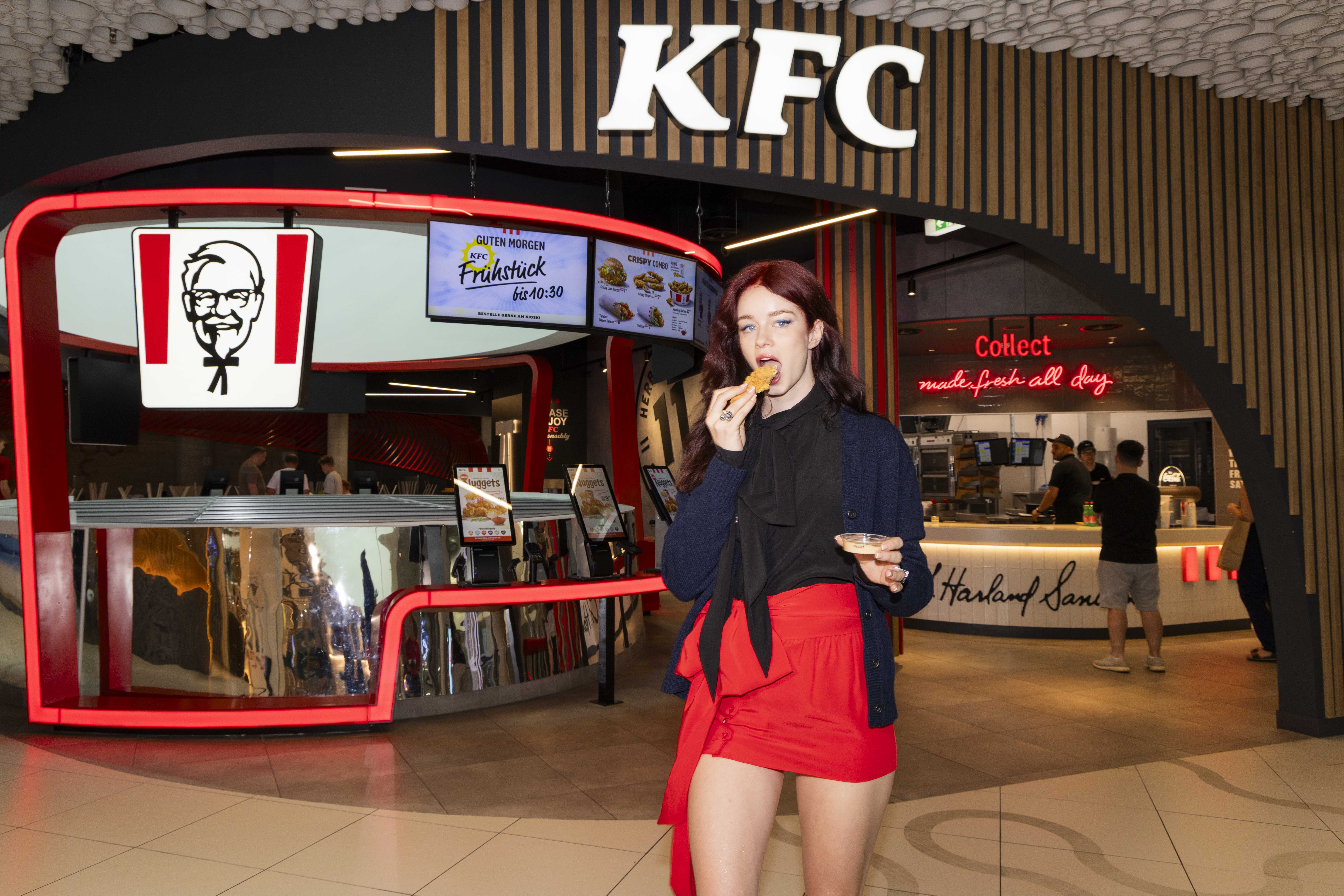 Frau mit rotem Rock isst KFC-Chicken vor dem Filialeingang im Einkaufszentrum