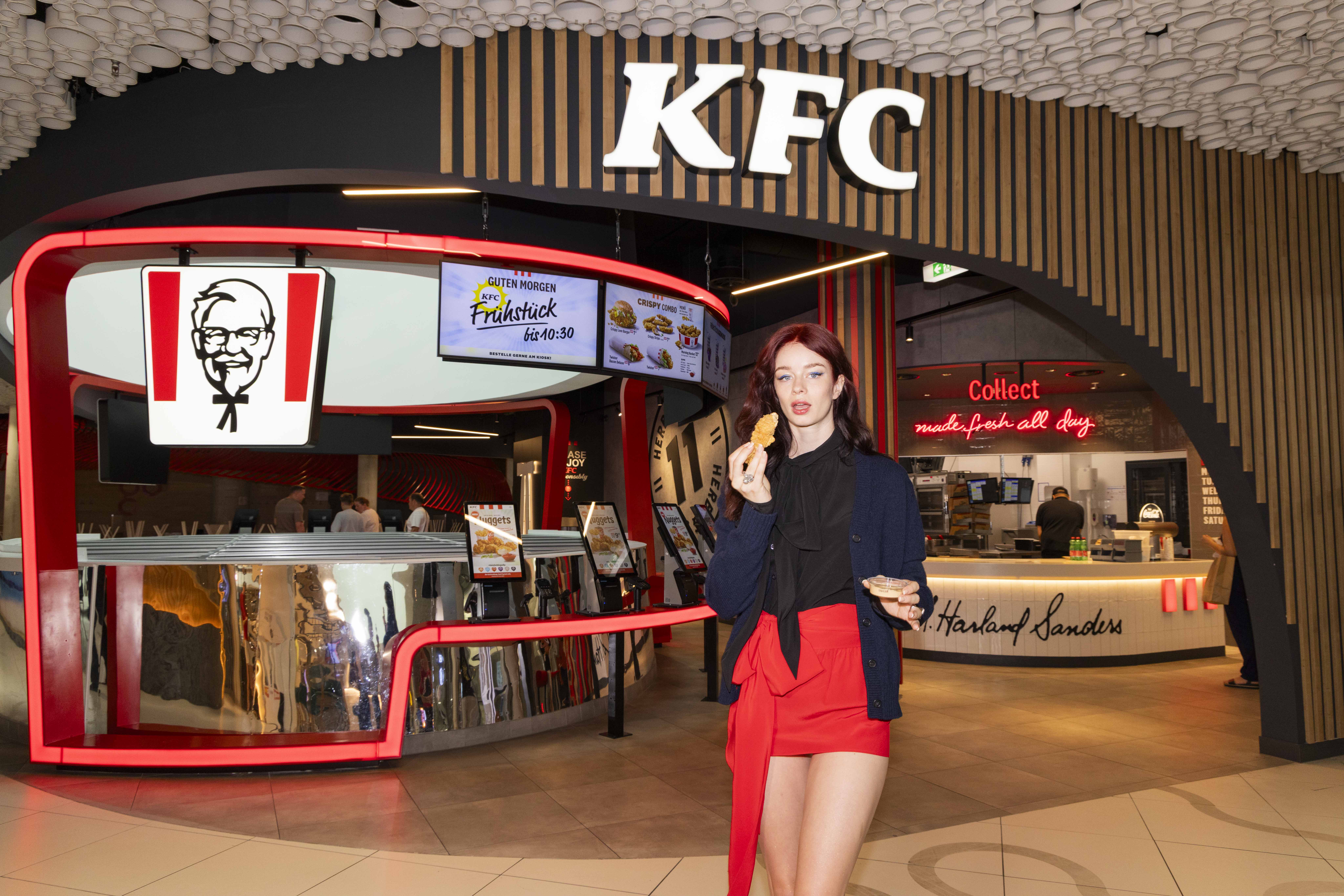 Frau isst Chicken-Snack vor der KFC-Theke im Einkaufszentrum