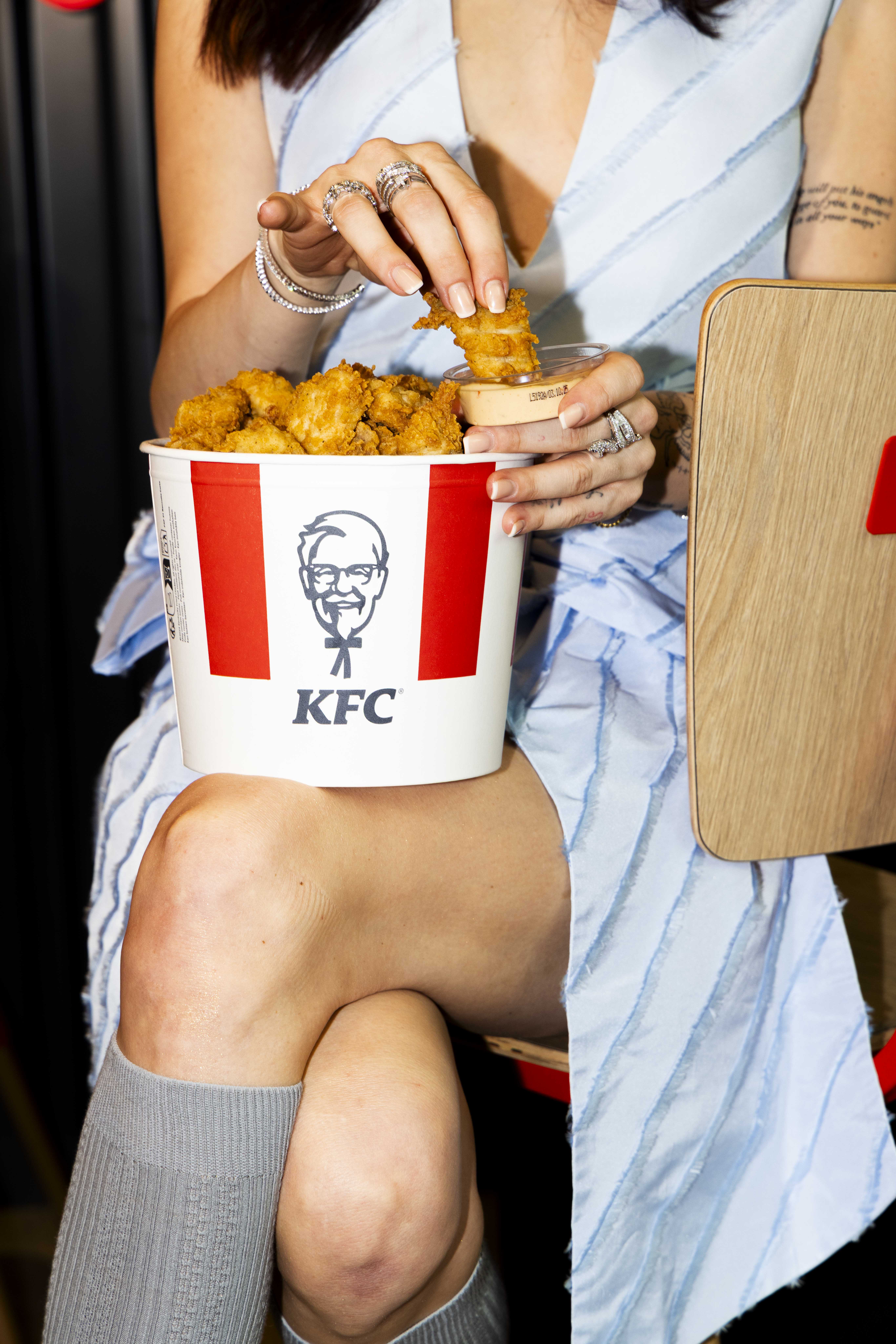 Nahaufnahme: Frau hält KFC-Chicken-Bucket auf dem Schoß