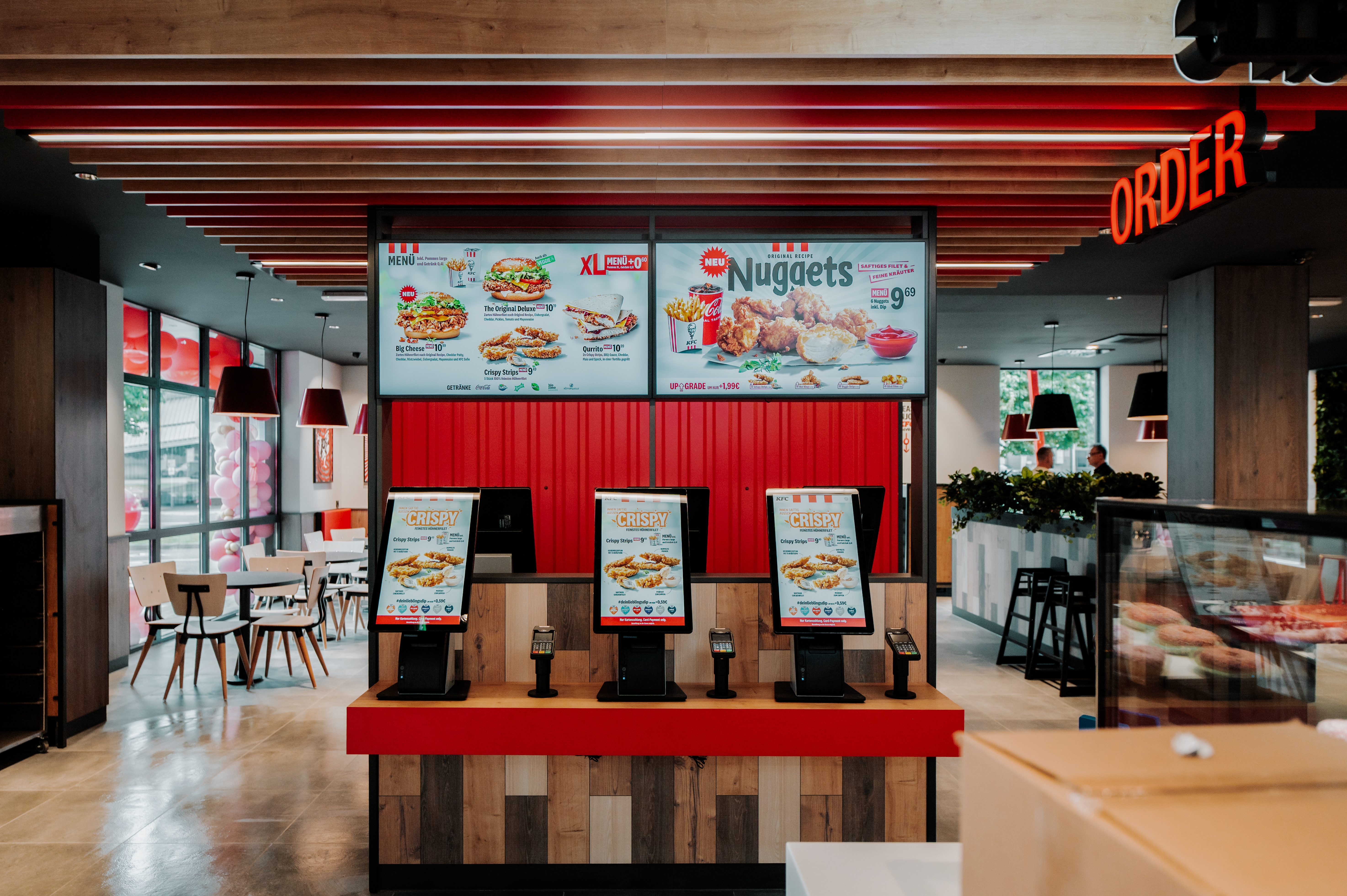 Selbstbedienungsterminals einer KFC-Filiale mit Werbetafel für Nuggets und Leuchtschrift 'Order'