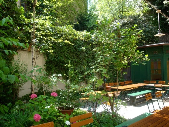 Grüner Biergarten im Innenhof mit Holztischen, Bänken und üppiger Efeubegrünung an der Wand