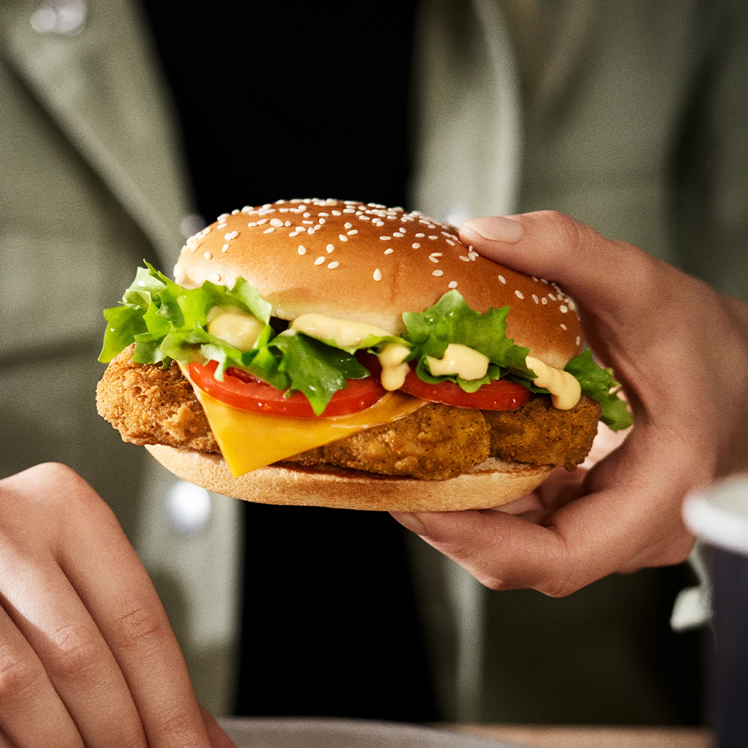 Zwei Hände halten einen KFC Veggie Burger mit paniertem Veggie-Patty, Cheddar, Tomate und Salat