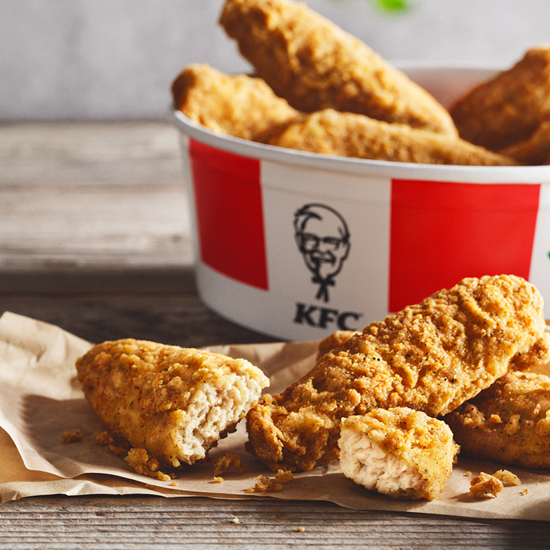 KFC Veggie Strips vor einem KFC Bucket, ein Strip aufgebrochen