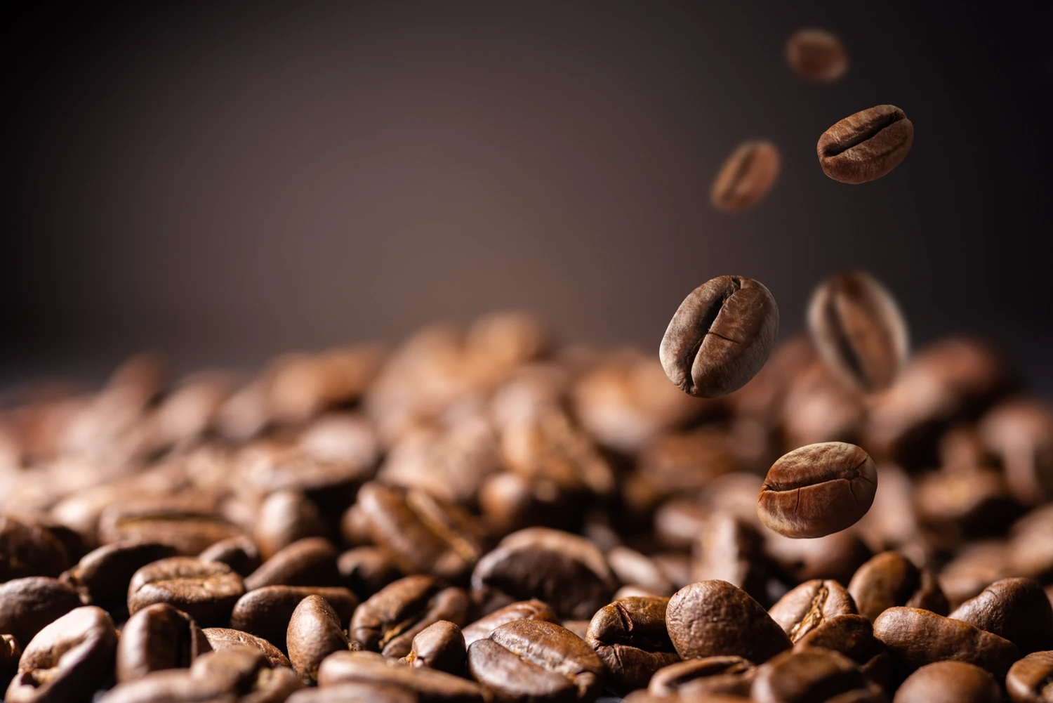 Geröstete Kaffeebohnen, einzelne Bohnen fallen vor dunklem Hintergrund darauf herab
