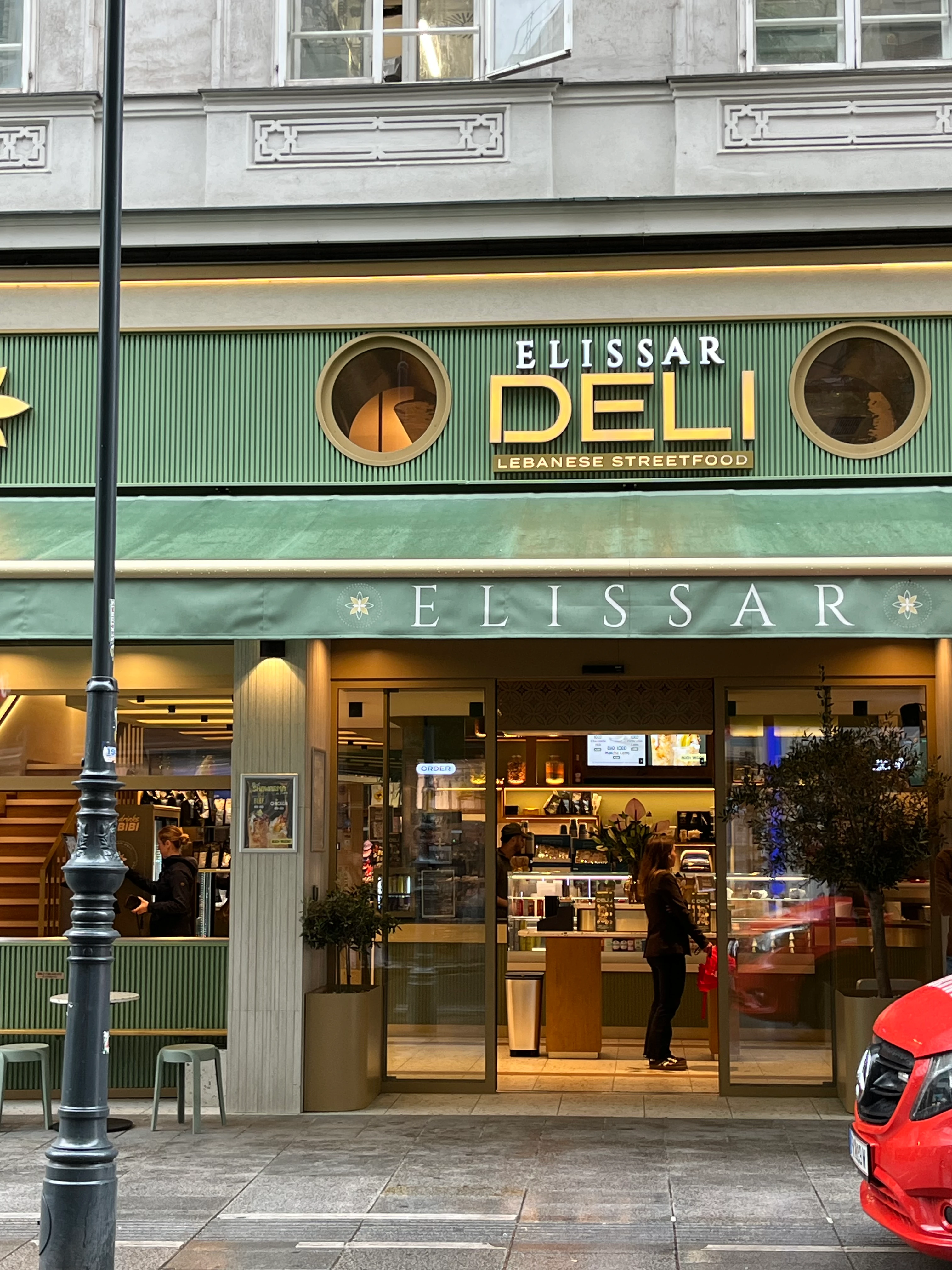 Außenansicht des Elissar Deli Restaurants mit grünem Schild und Glasfassade
