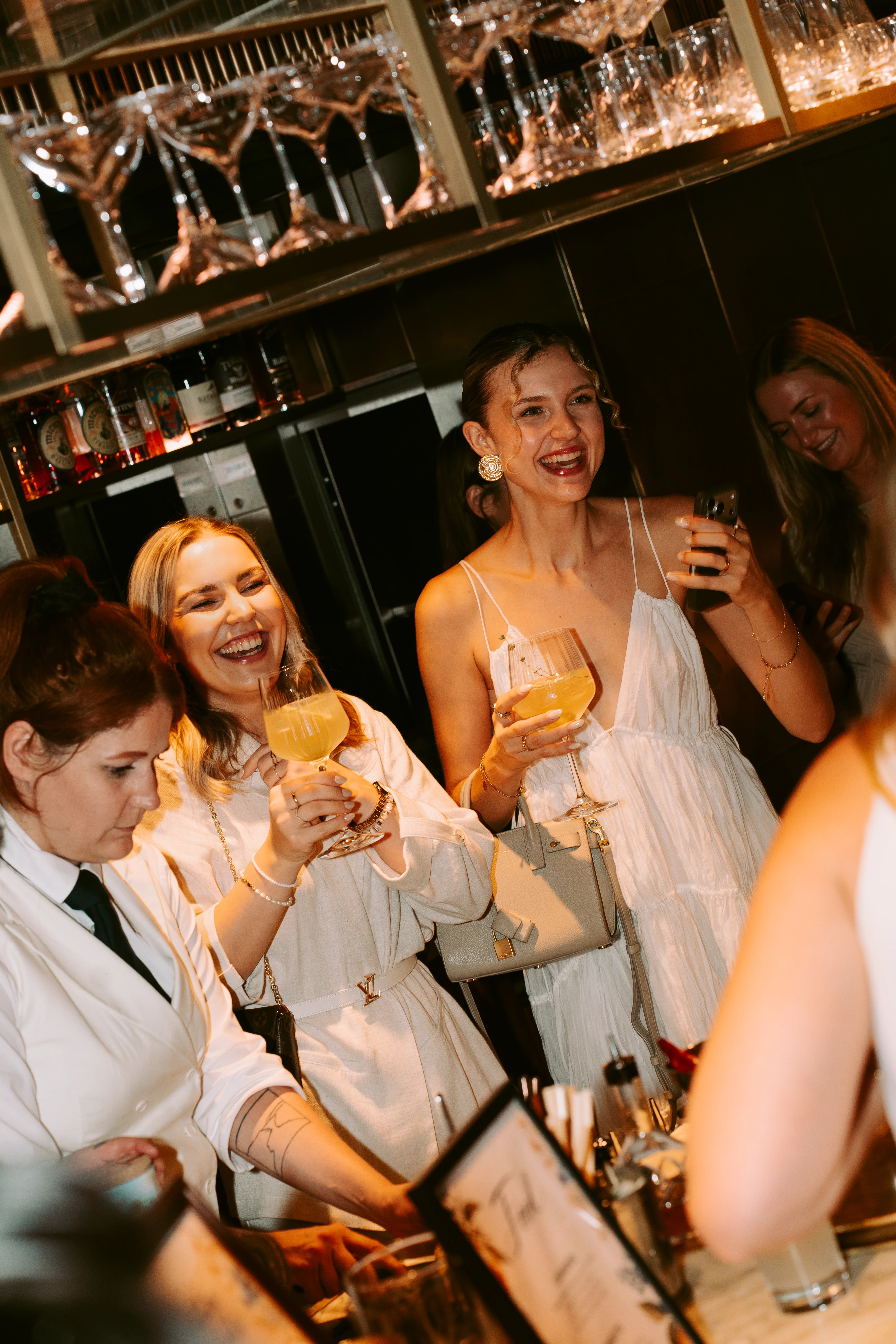 Gruppe gut gelaunter Frauen feiert in einer Bar und stößt mit Cocktails an.