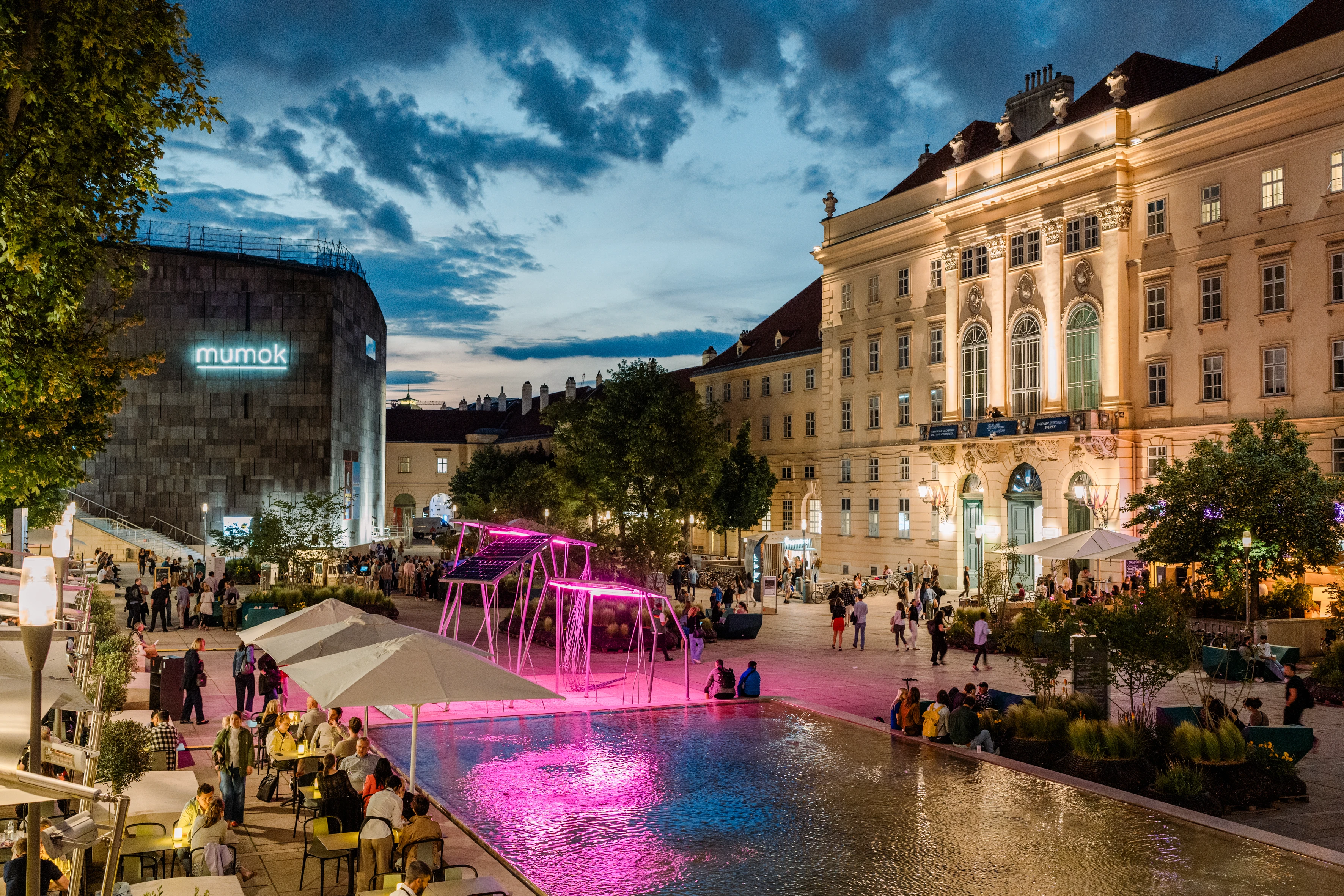 Abendstimmung im Museumsquartier in Wien mit beleuchteten Gebäuden, dem Mumok und Menschen auf dem Platz.