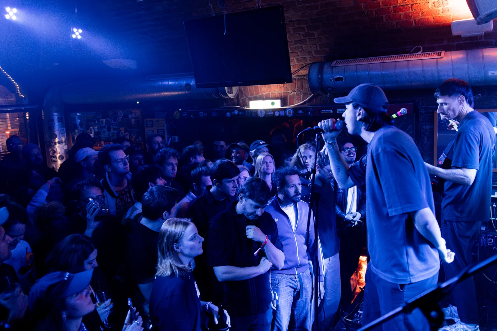 Sänger mit Mikrofon bei einem Live-Konzert vor einem Club-Publikum unter blauem Bühnenlicht
