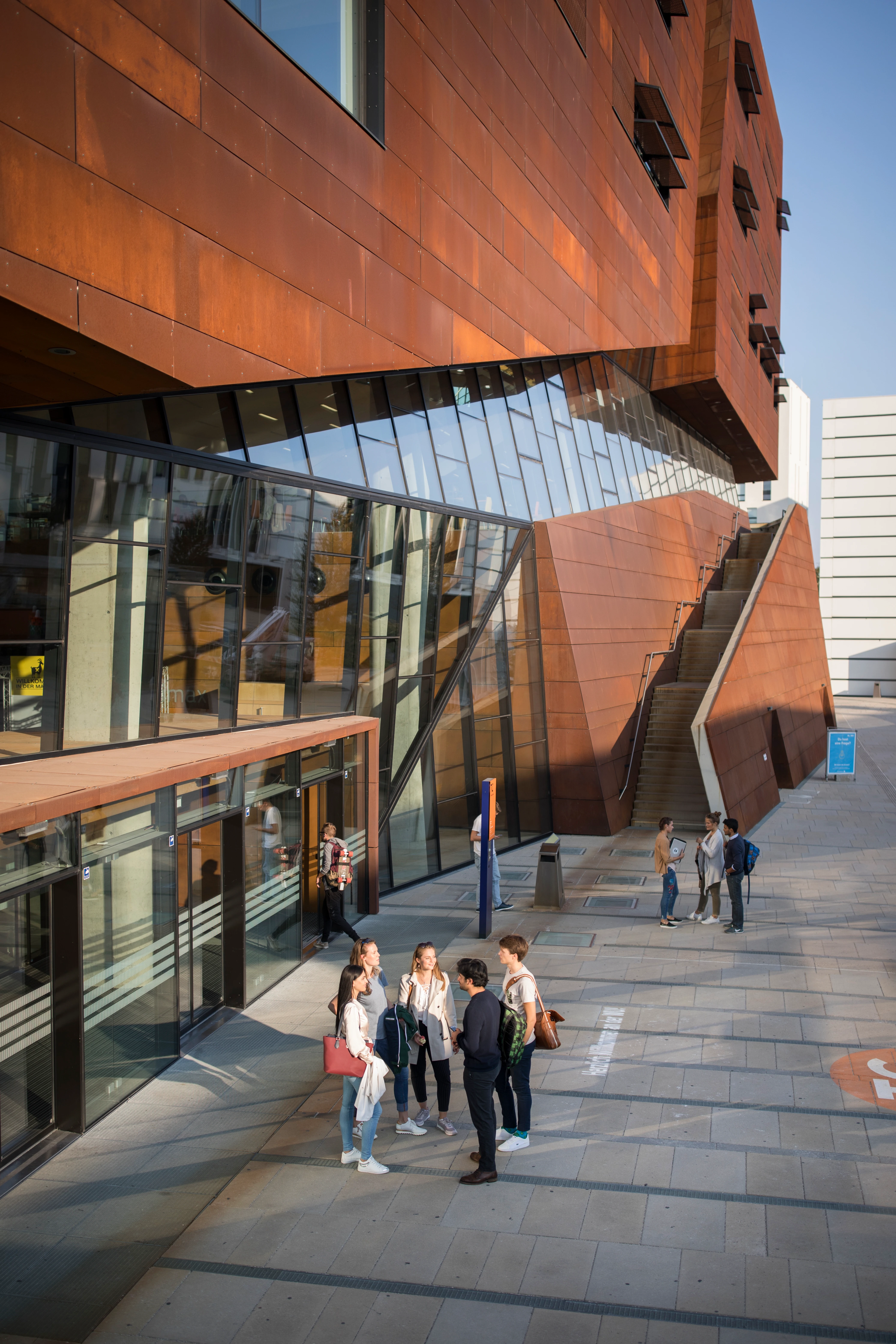 Gruppe von Studenten im Gespräch vor moderner Universitätsarchitektur mit rostbrauner Fassade