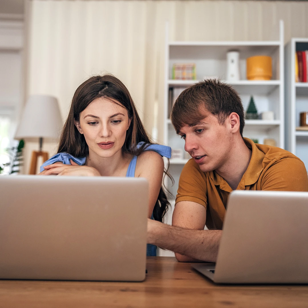 Junges Paar sitzt in der Wohnung vor Laptops und arbeitet zusammen im Homeoffice.