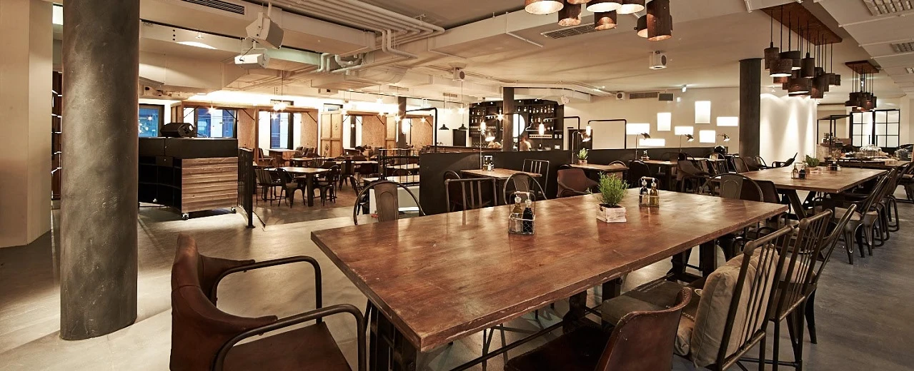 Modernes Restaurant mit großen Holztischen, gemütlichen Stühlen und stimmungsvoller Beleuchtung im Innenbereich.