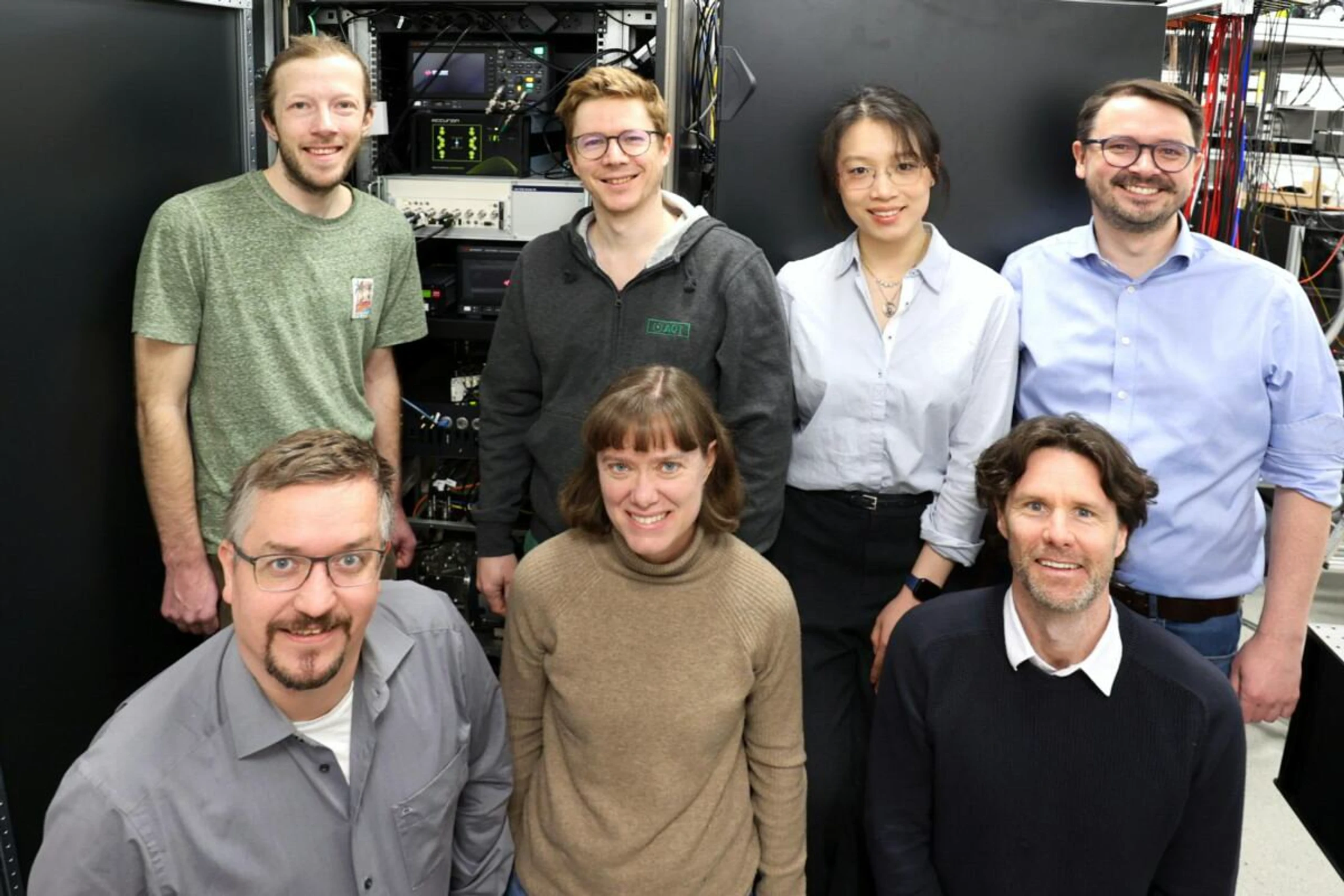 Das Innsbrucker Forschungskonsortium um Pascal Wintermeyer, Josef Schupp, Moming Jia, Juris Ulmanis (hinten v.l.) und Thomas Monz, Tracy Northup, Ben Lanyon (vorne v.l.) vor dem kompakten Quantencomputer-Prototyp