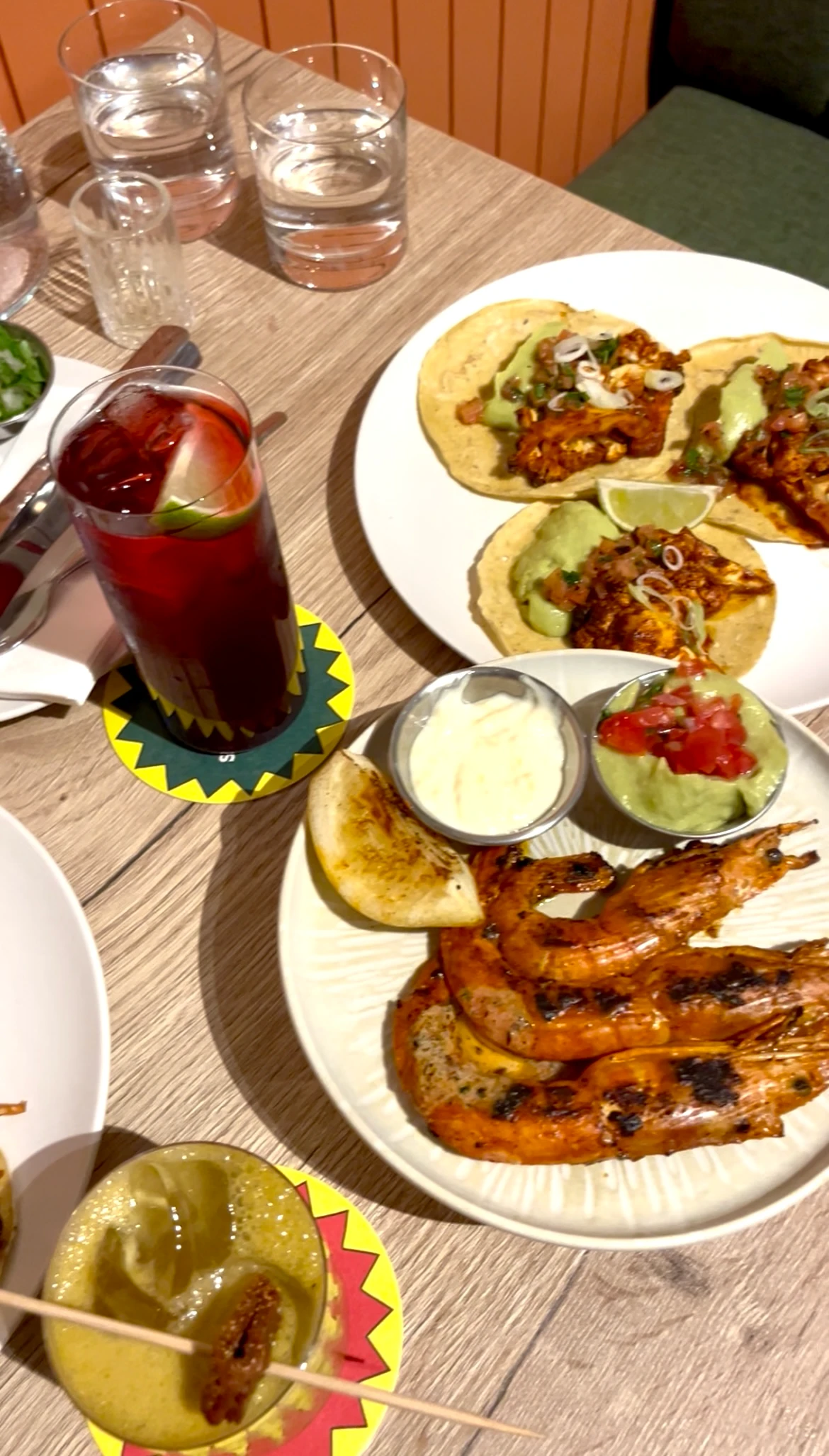 Tisch mit mexikanischem Essen wie Tacos, gegrillten Garnelen, Guacamole und roten Cocktails.