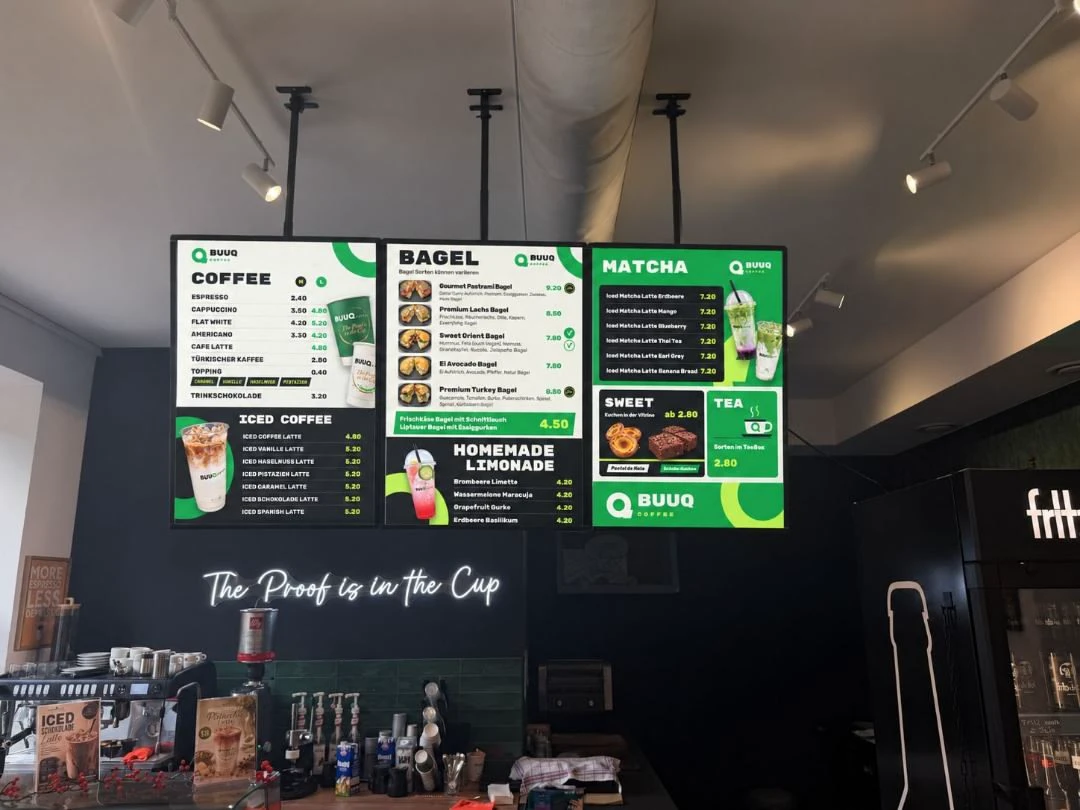 Digitale Menütafeln in einem Café mit Kaffeespezialitäten, Bagels, Matcha und Limonaden sowie Preisen.