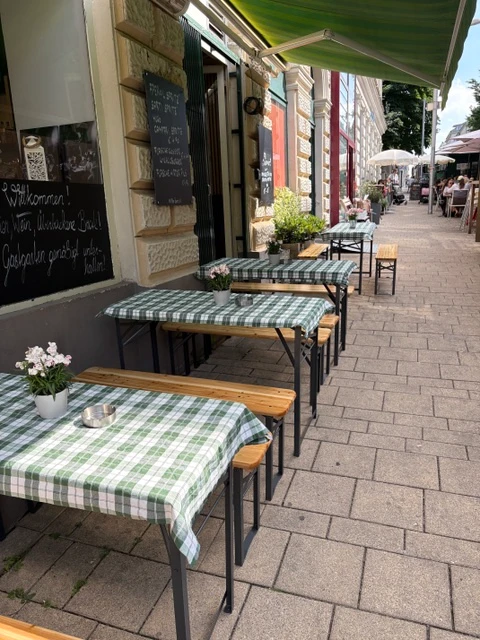Gemütlicher Außenbereich eines Cafés mit grün-weiß karierten Tischen und Holzbänken in einer Fußgängerzone.