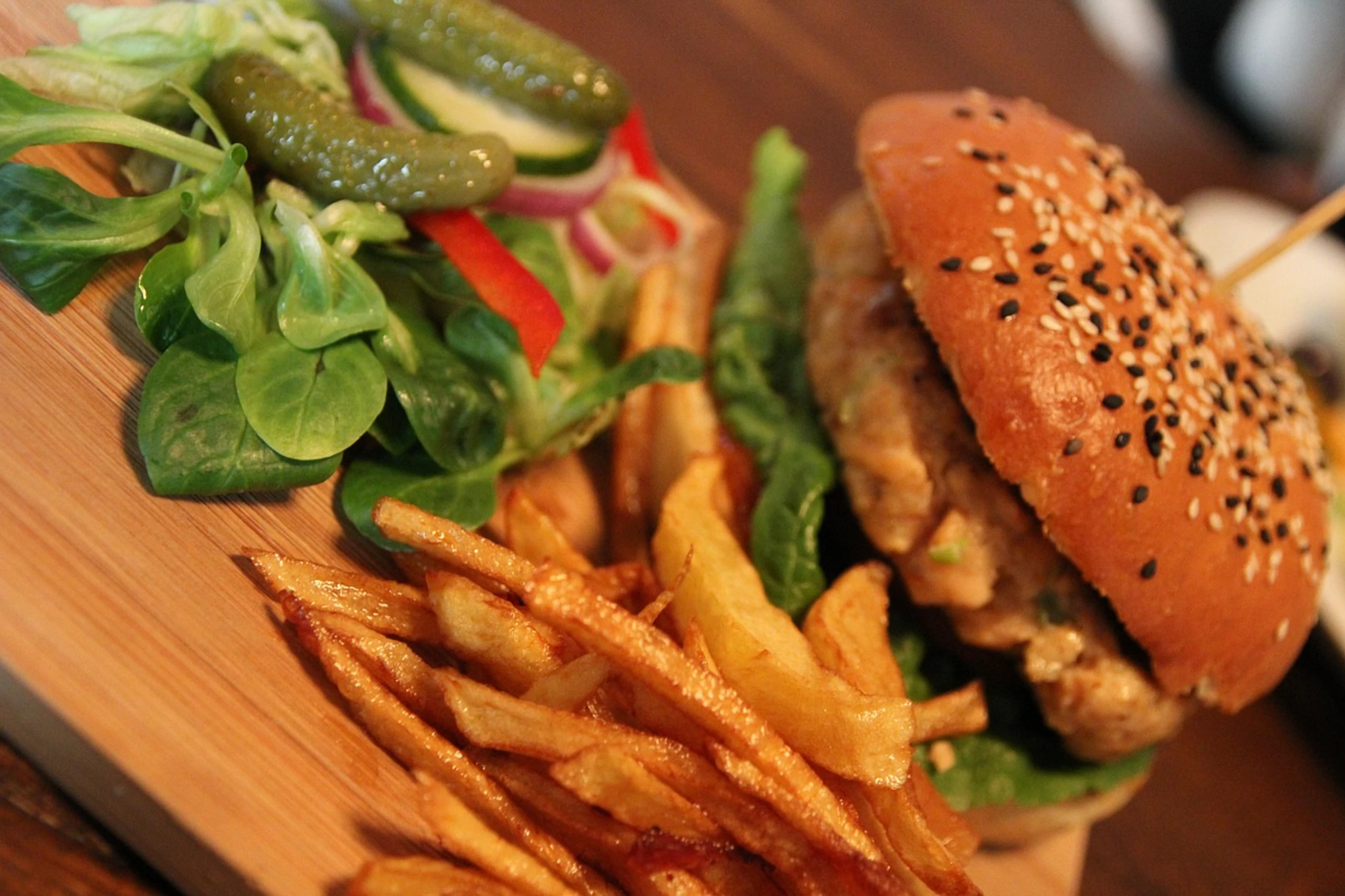 Burger mit Pommes frites und Salat auf einem Holzbrett