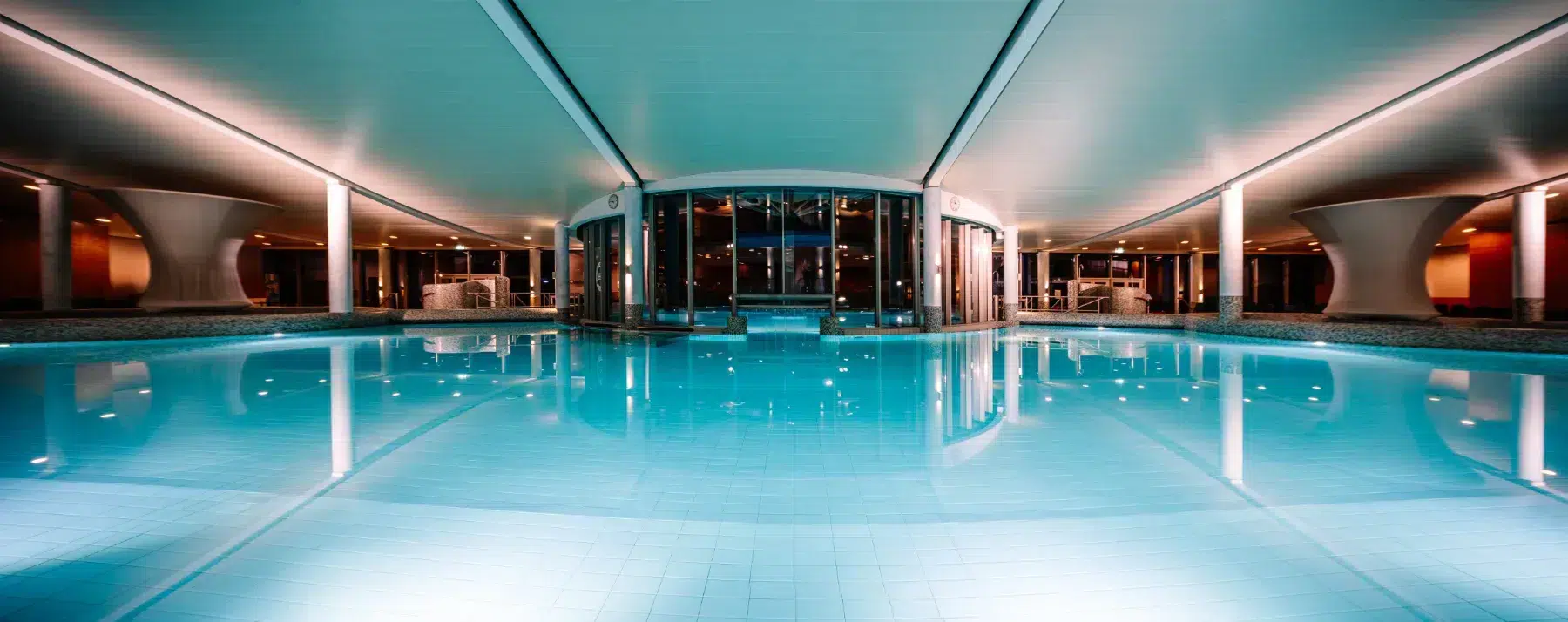 Modernes Hallenschwimmbad mit klarem blauen Wasser und stimmungsvoller Beleuchtung in einem Wellnessbereich