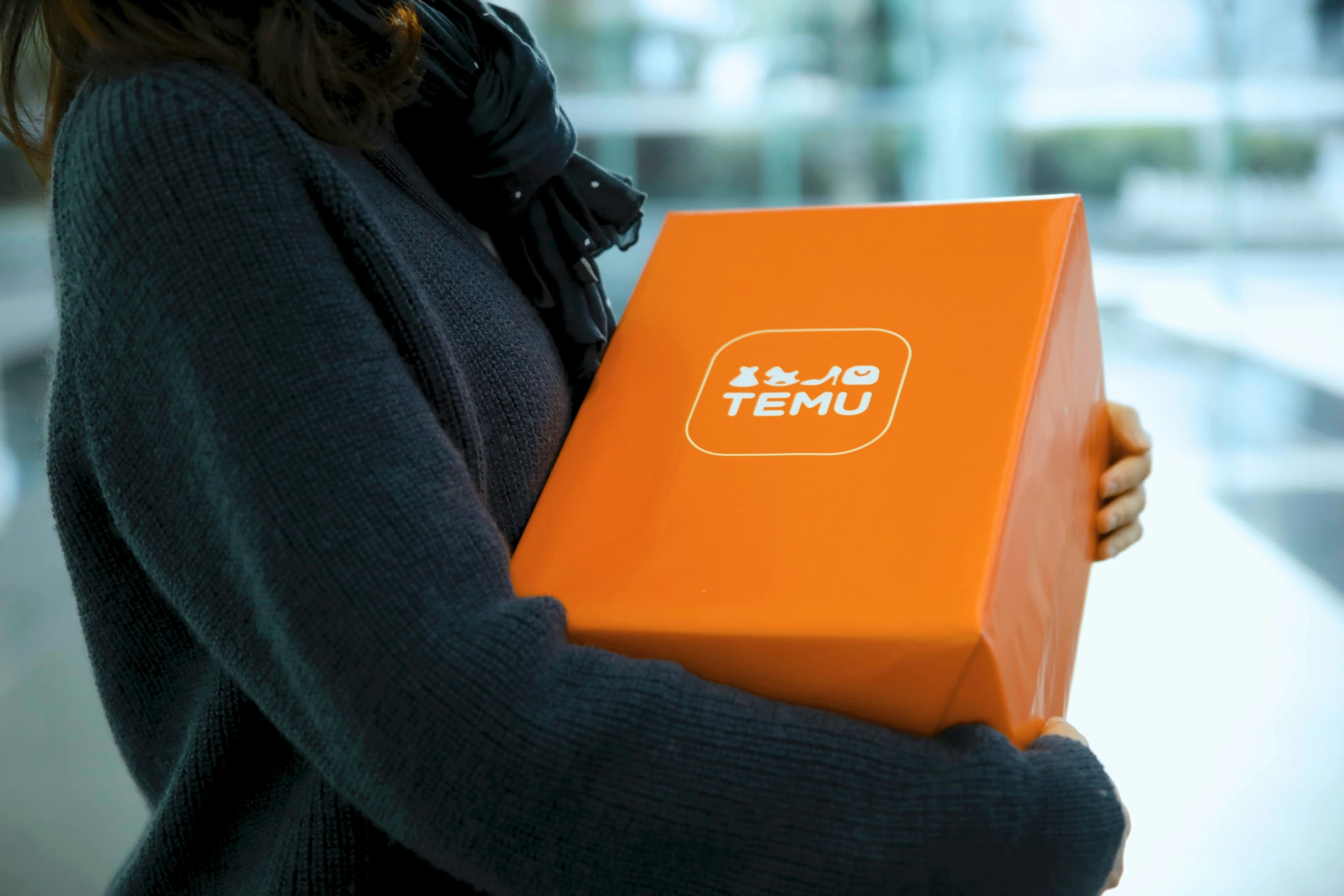 Frau hält ein orangefarbenes Paket des Onlinehändlers Temu