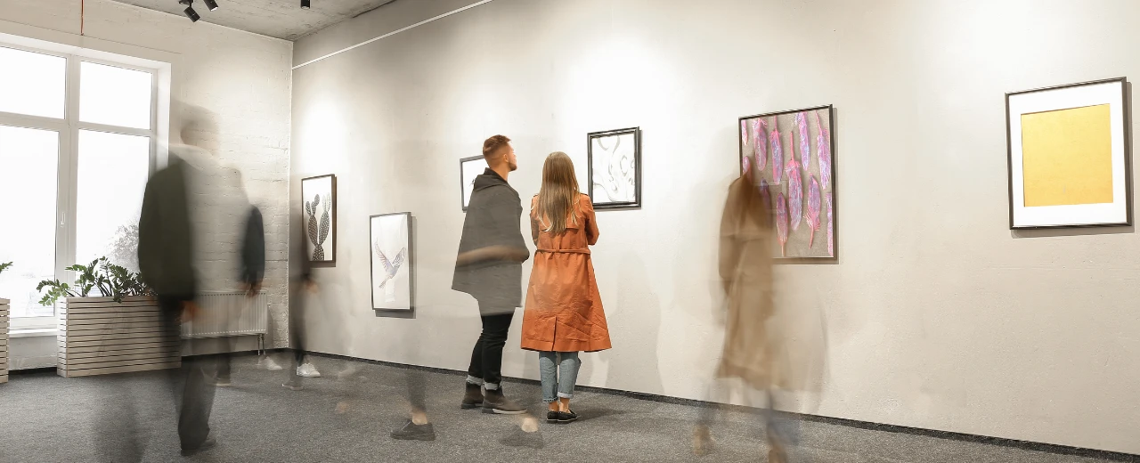 KunstKulturMai Header: Paar betrachtet Kunstwerke in moderner Galerie.  Unscharfe Besucher im Hintergrund.