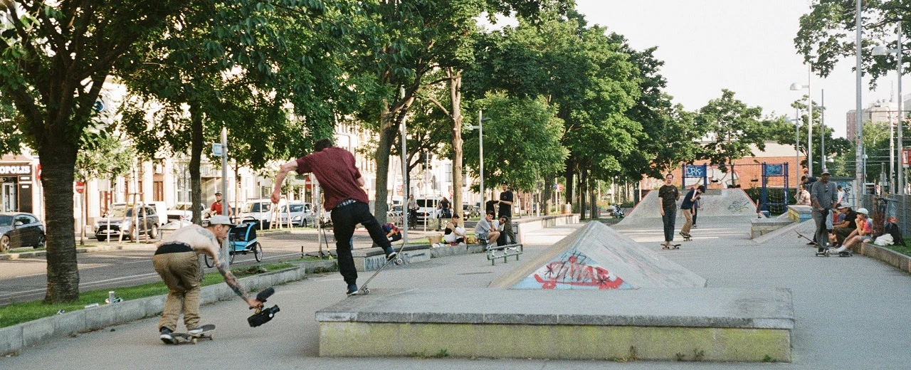 Mehrere Skater in einem urbanen Skatepark an einem sonnigen Tag. Skateboards und Rampen sind zu sehen.