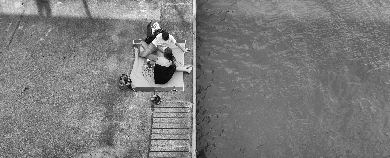 Schwarz-weiß Foto: Paar sitzt entspannt auf einer Decke am Fluss.  Bearbeitet mit Adobe Lightroom.