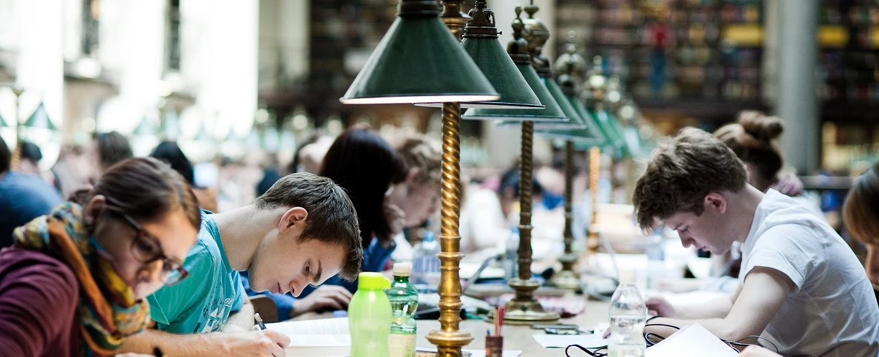 Konzentrierte Studenten lernen in einer historischen Bibliothek mit antiken Schreibtischlampen.