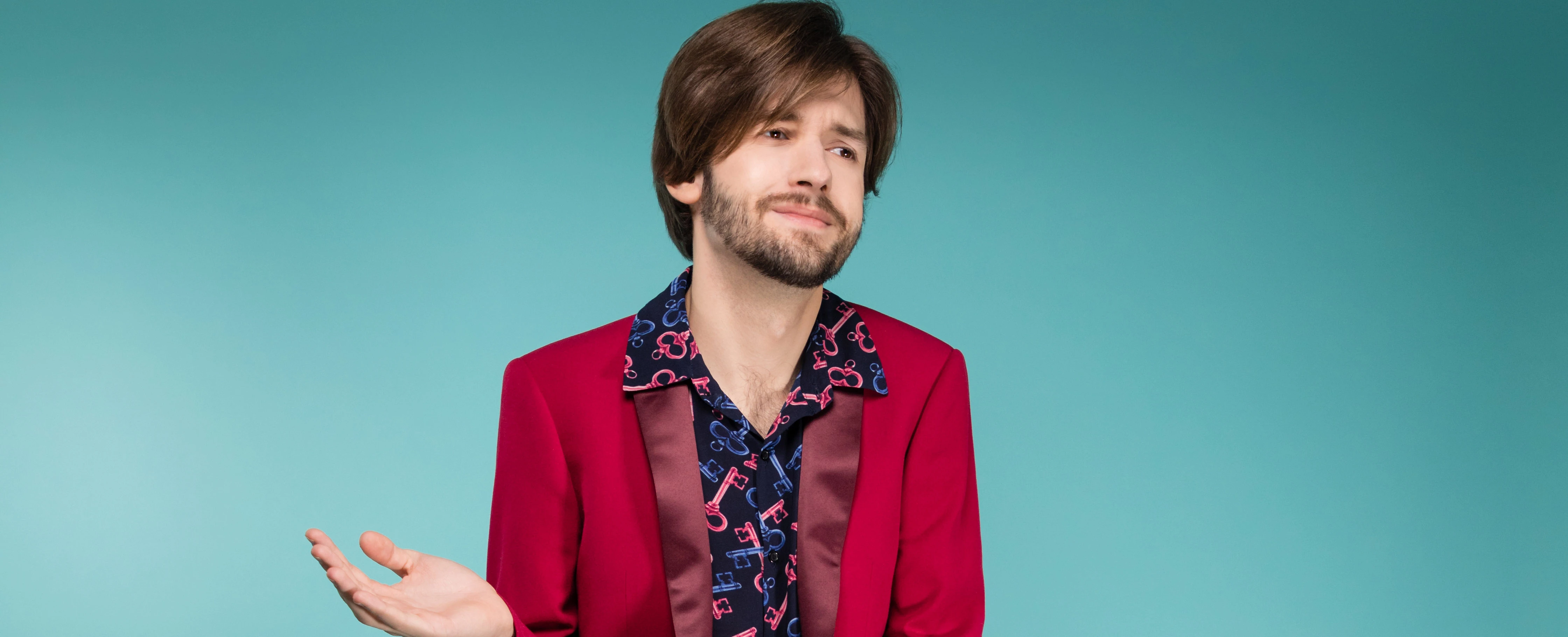 © Dominik Pichler Porträt eines jungen Mannes mit rotem Blazer und Schlüsselmuster-Hemd vor hellblauem Hintergrund. Bearbeitet mit Adobe Lightroom.