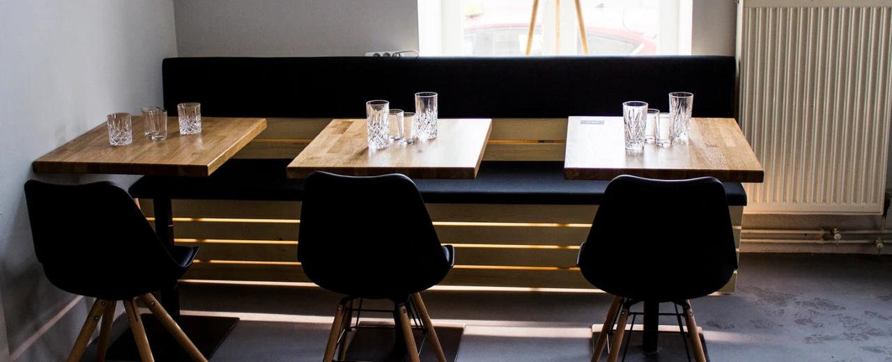 Moderne Restaurant-Ecke: 3 Holztische, schwarze Stühle & Bank.