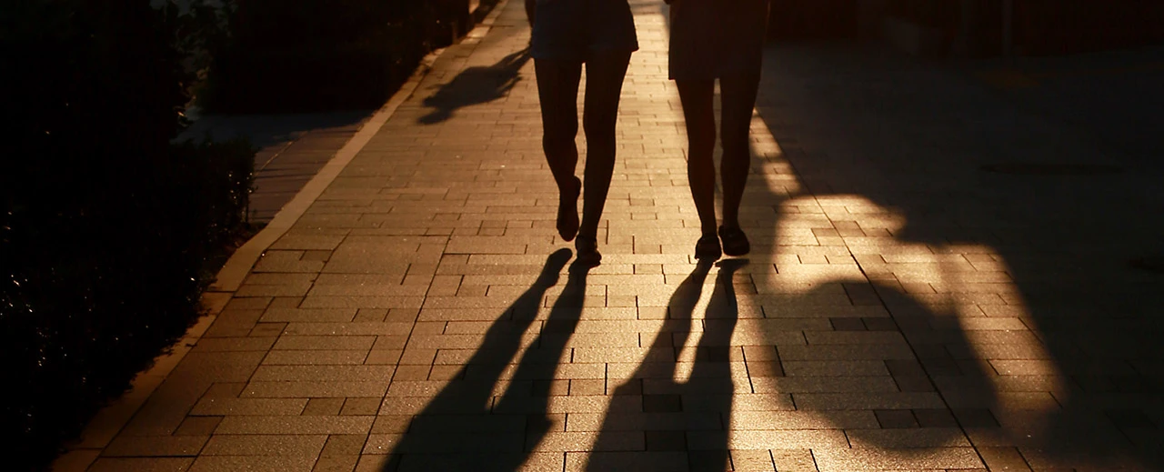 © unsplash.com adamara Zwei Personen gehen abends über einen beleuchteten Gehweg. Ihre langen Schatten sind deutlich sichtbar.