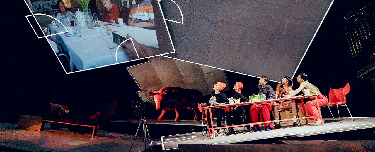 Schauspieler auf Bühne mit rotem Stier & Familienprojektion.