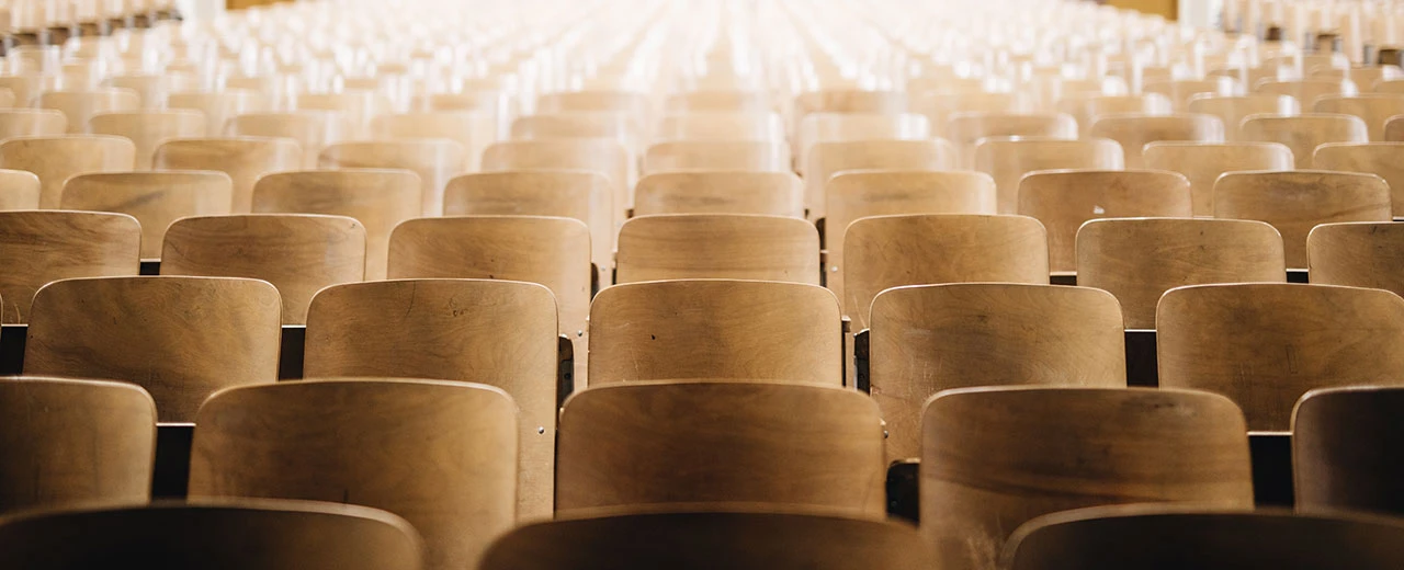 © Goodnight.at Leere Reihen von Holzstühlen in einem Auditorium, bereit für die nächste Veranstaltung.