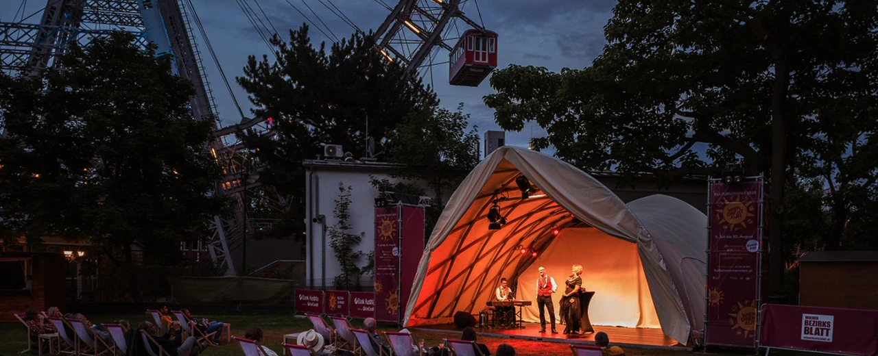 © Renée del Missier Open-Air Konzert mit Live-Musik unter einem Zelt vor Publikum und einem Riesenrad im Hintergrund.