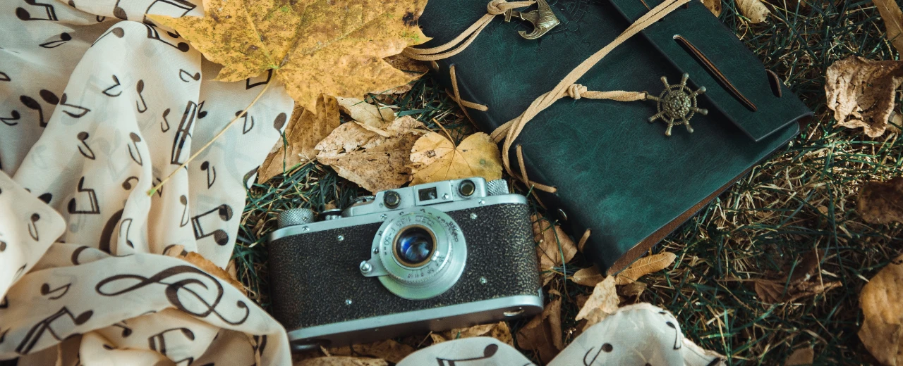 Vintage-Kamera, Ledernotizbuch und Noten-Schal auf Herbstlaub. Nostalgische Herbst-Szene.