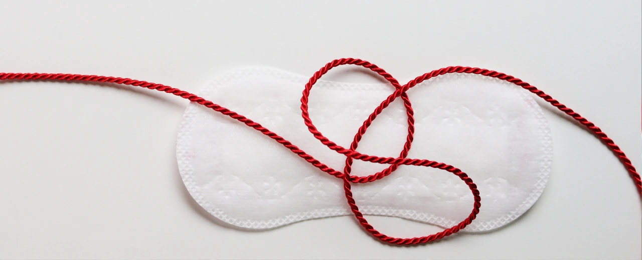 Rote Kordel auf Damenbinde; Konzept Menstruation, weibliche Gesundheit.