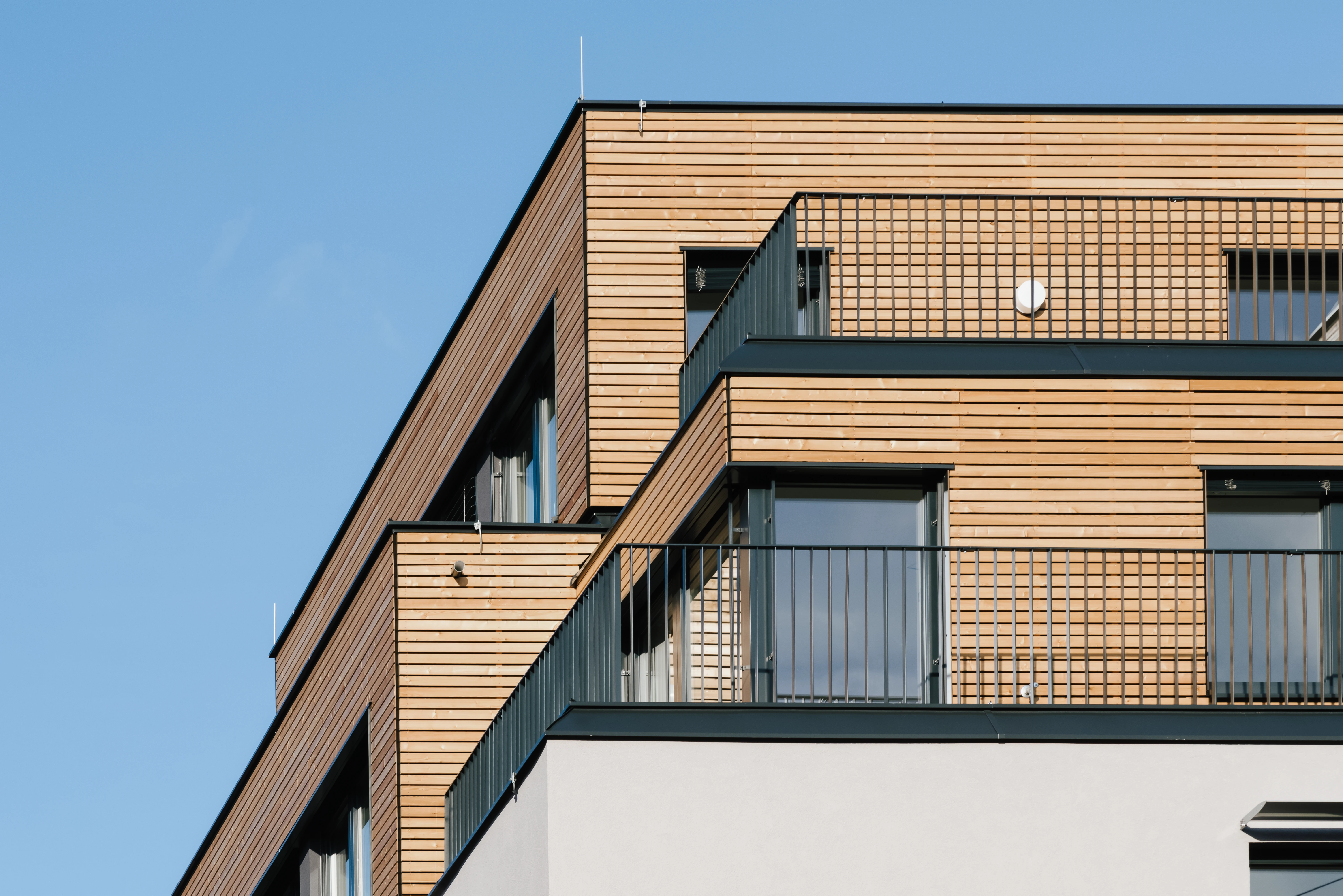 Blick auf obere Stockwerke eines Wohninvestments mit Holzfassade und schwarzen Metallbalkonen
