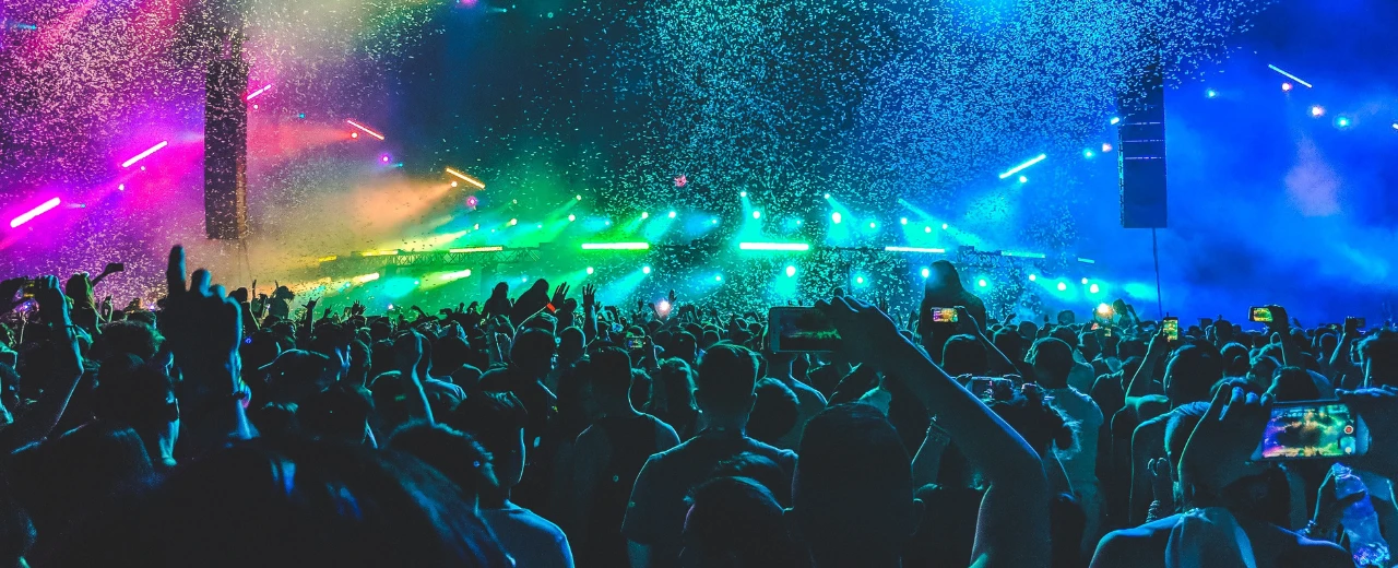 Konzerthighlights: Eine große jubelnde Menschenmenge vor einer mit bunten Lichtern und Konfetti erleuchteten Bühne.