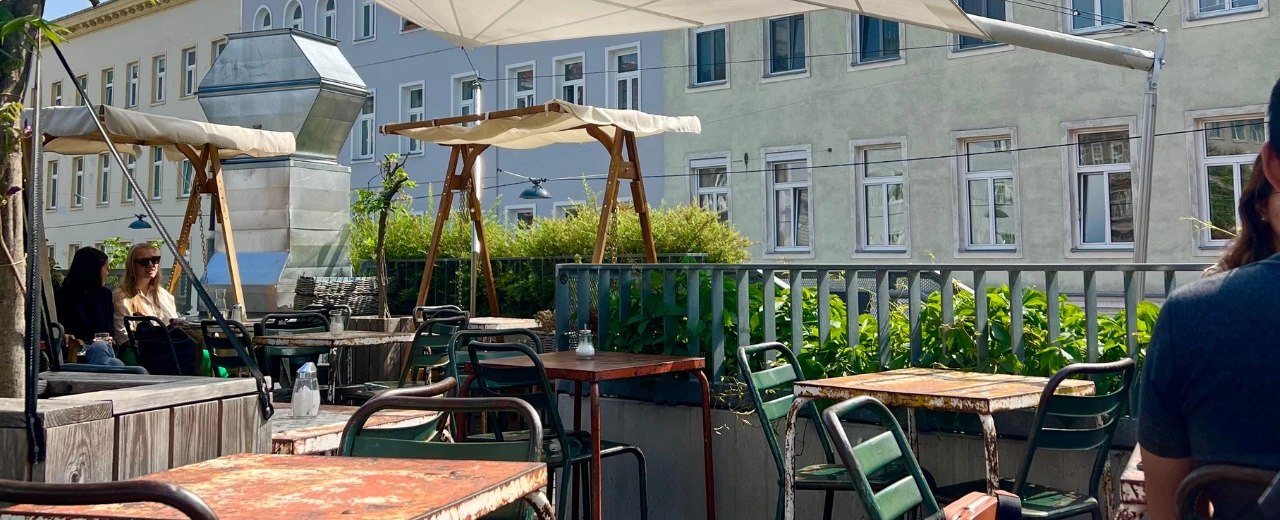 Gemütliche Außenterrasse eines Cafés mit rostigen Tischen und Stühlen unter Sonnenschirmen.