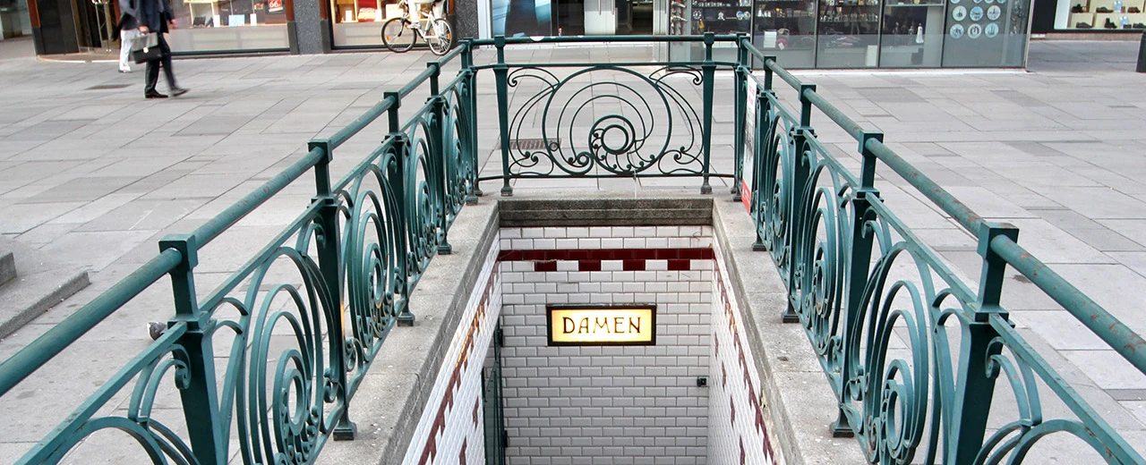 Öffentlicher Toiletteneingang für Damen mit grünem Geländer und weißen Kacheln. Erstellt mit Adobe Photoshop.