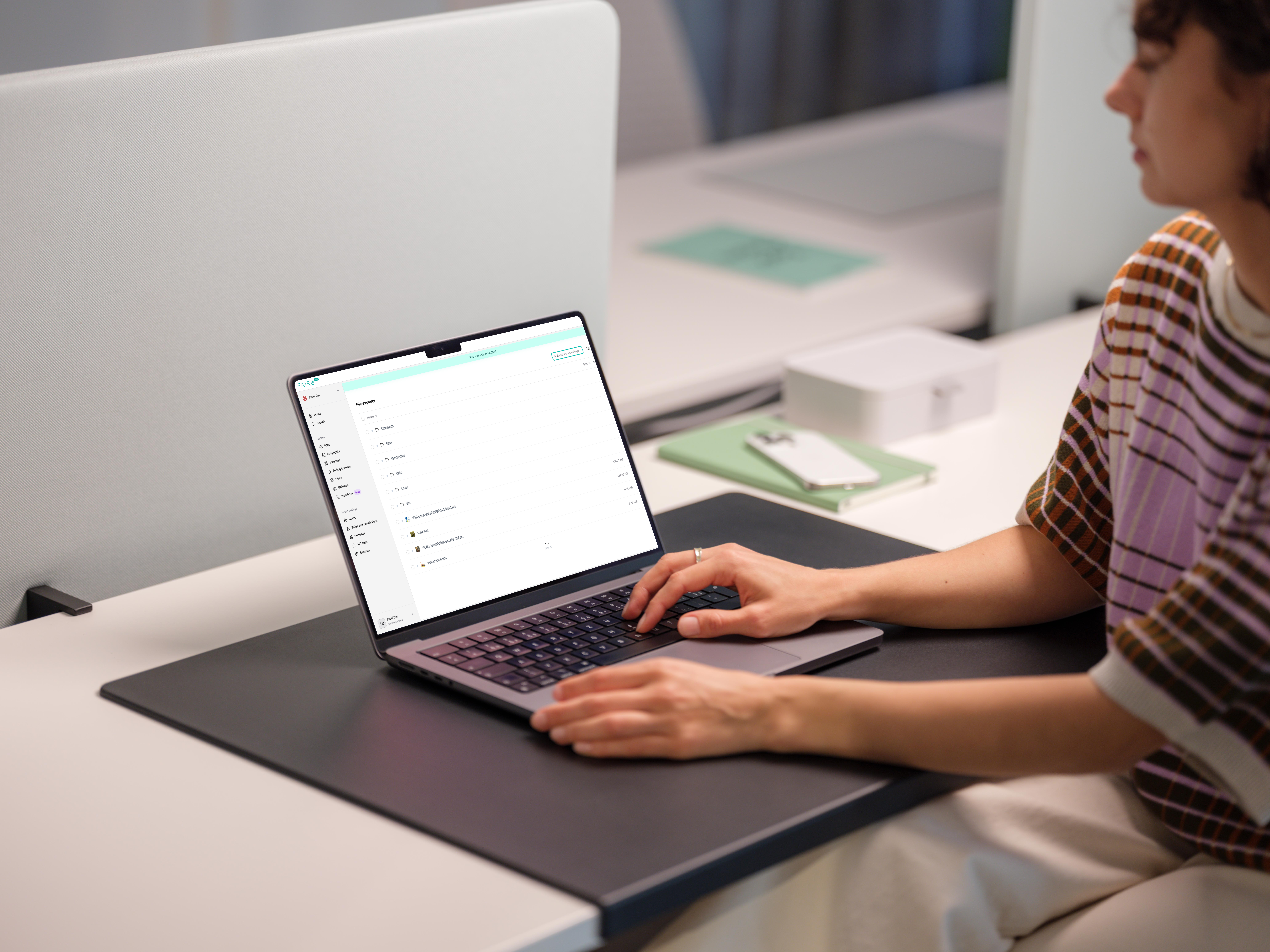 A woman sitting at an office desk using a laptop to browse a file explorer interface.