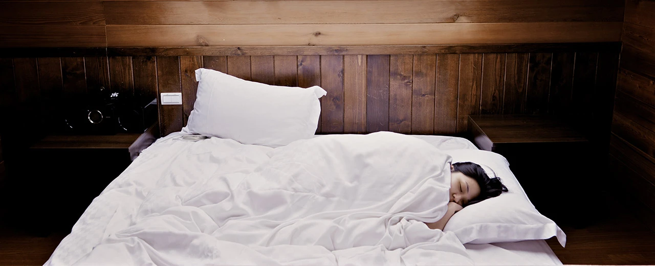 Frau schläft ruhig in einem Bett mit weißem Leinen in einem Schlafzimmer mit Holzwänden.