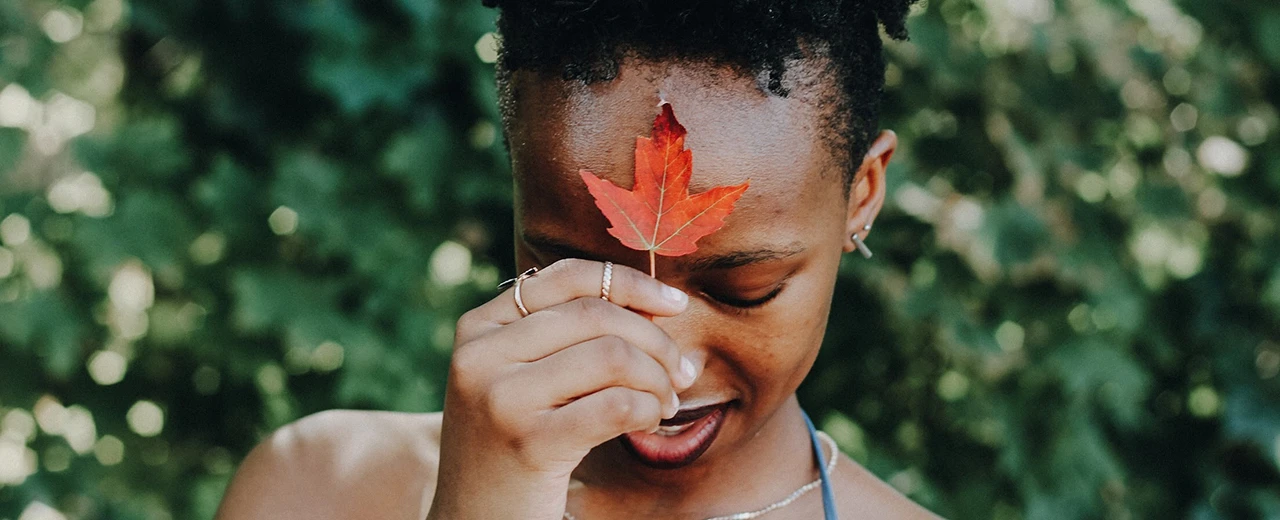 © unsplash Nahaufnahme einer Frau mit rotem Ahornblatt auf der Stirn vor grünem Hintergrund. Herbst, Natur, Schönheit.