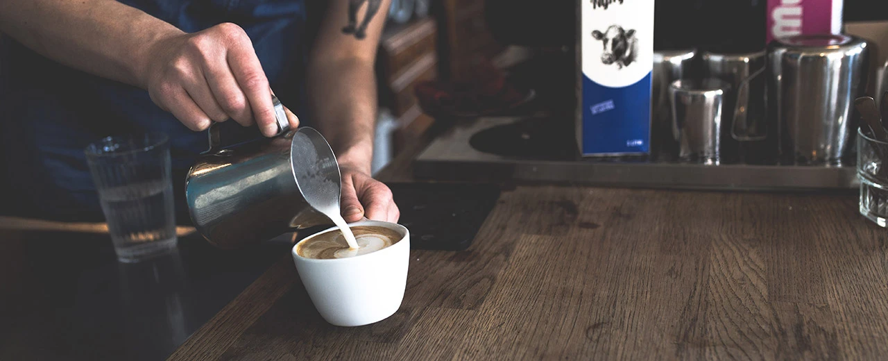 Barista gießt Milch in einen Cappuccino, Latte Art, Kaffeehaus, Getränk, Kaffee